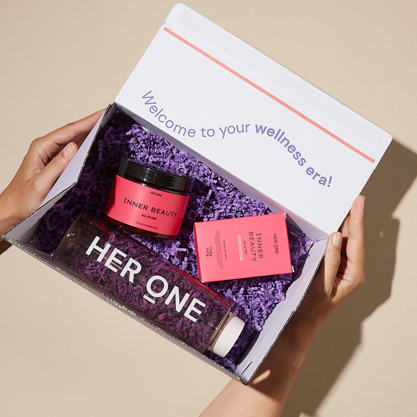 Produkte der Marke „HER ONE in einer Schachtel und der Satz “Welcome to your wellness era" auf der Schachtel