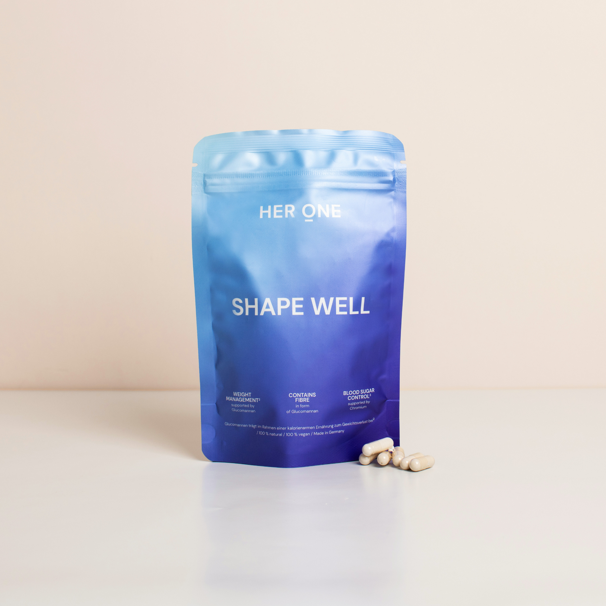 Ein blaues Produktbeutel mit der Aufschrift "Shape Well" und einigen weißen Kapseln davor auf einem Tisch.