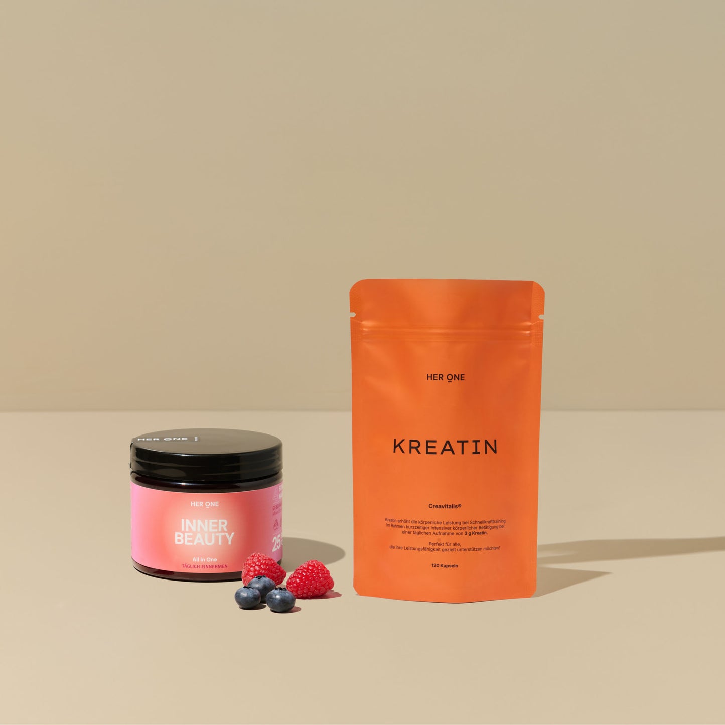 Ein Glas "Inner Beauty" und eine Packung "Kreatin" von "Her One" mit Himbeeren und Blaubeeren auf beigem Hintergrund.