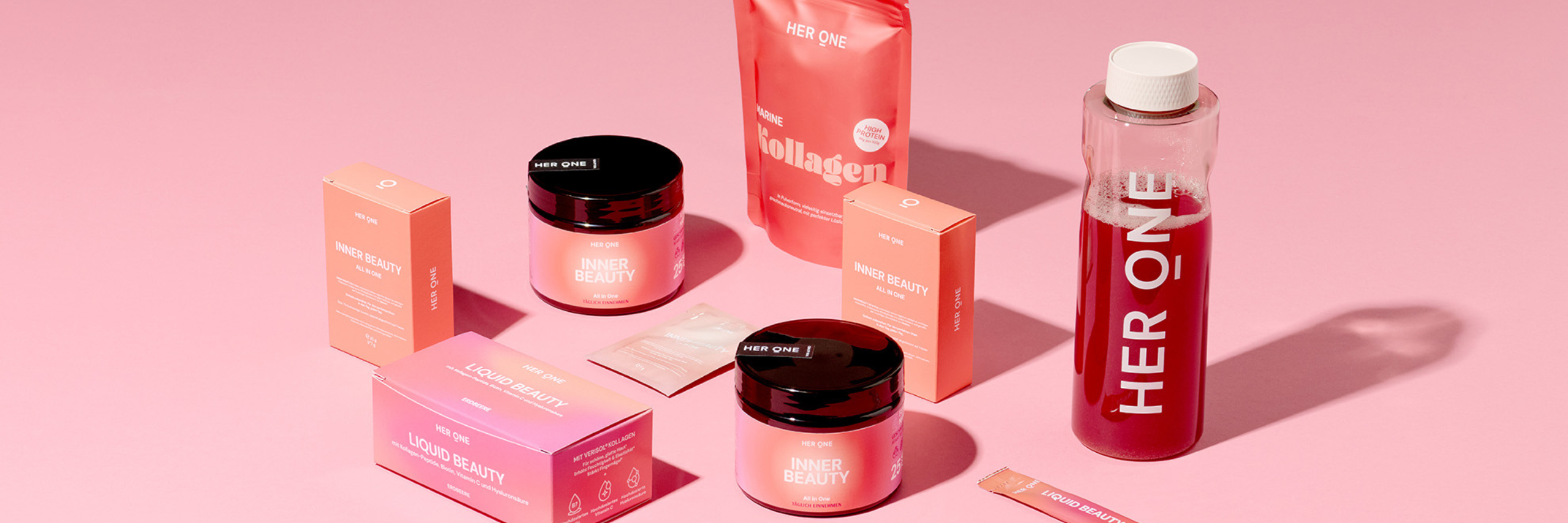 Cosmetic products on a pink background, including cans, boxes and a drink labeled "HER ONE".