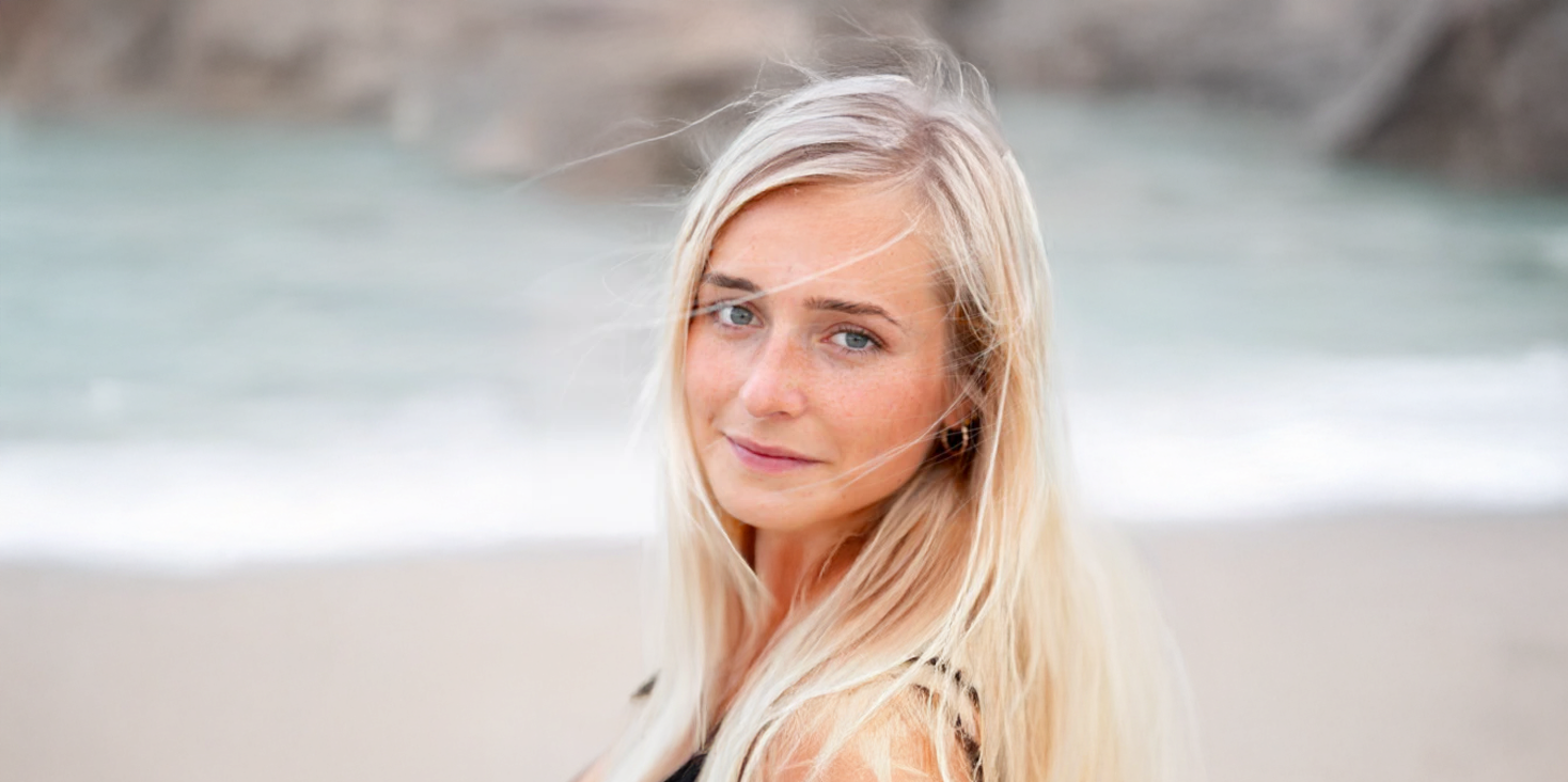 Woman with blonde hair smiles slightly on the beach.