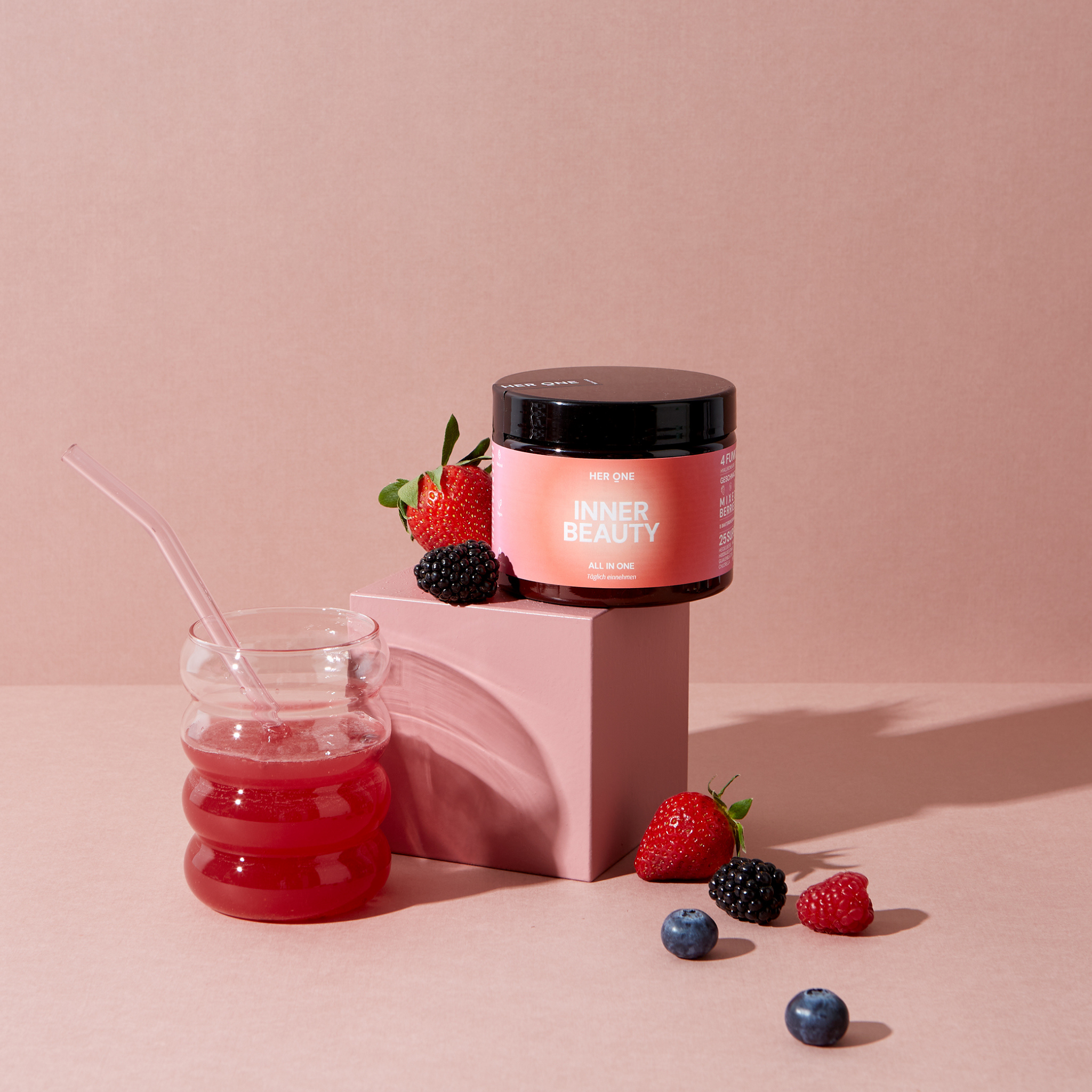 A jar of pink liquid, a pink tin with "Inner Beauty" and fruit on a pink background.