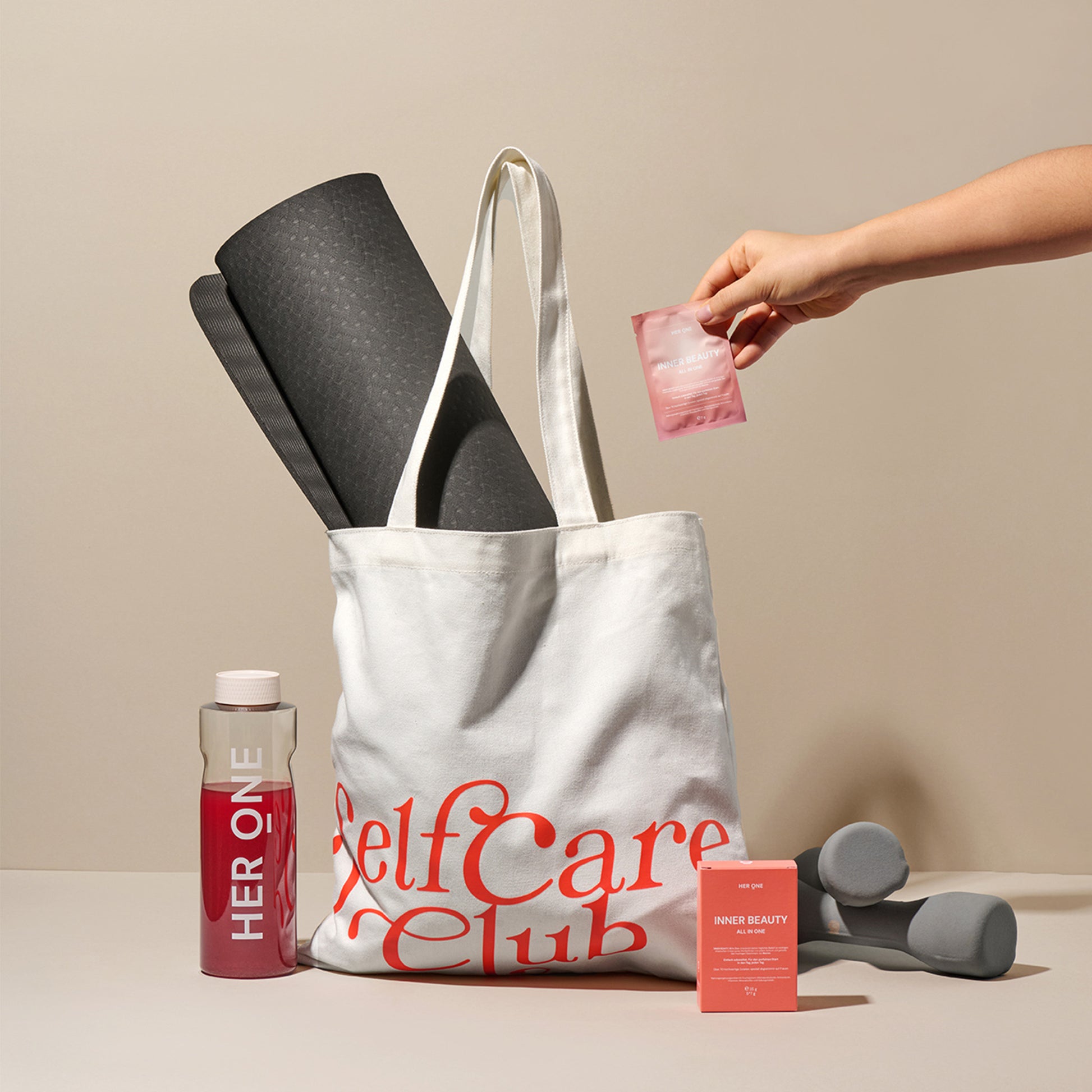 Cloth bag with yoga mat, drinks bottle, hand weights and a pink pack held by one hand.