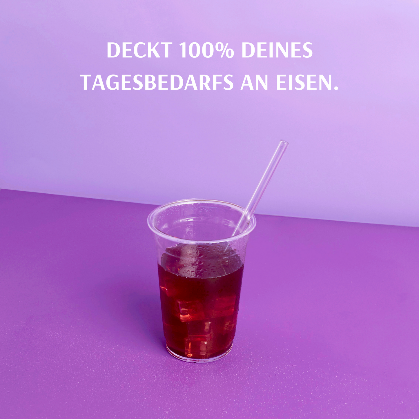 A plastic cup with a red drink and straw stands on a purple background with an advertising slogan above it.
