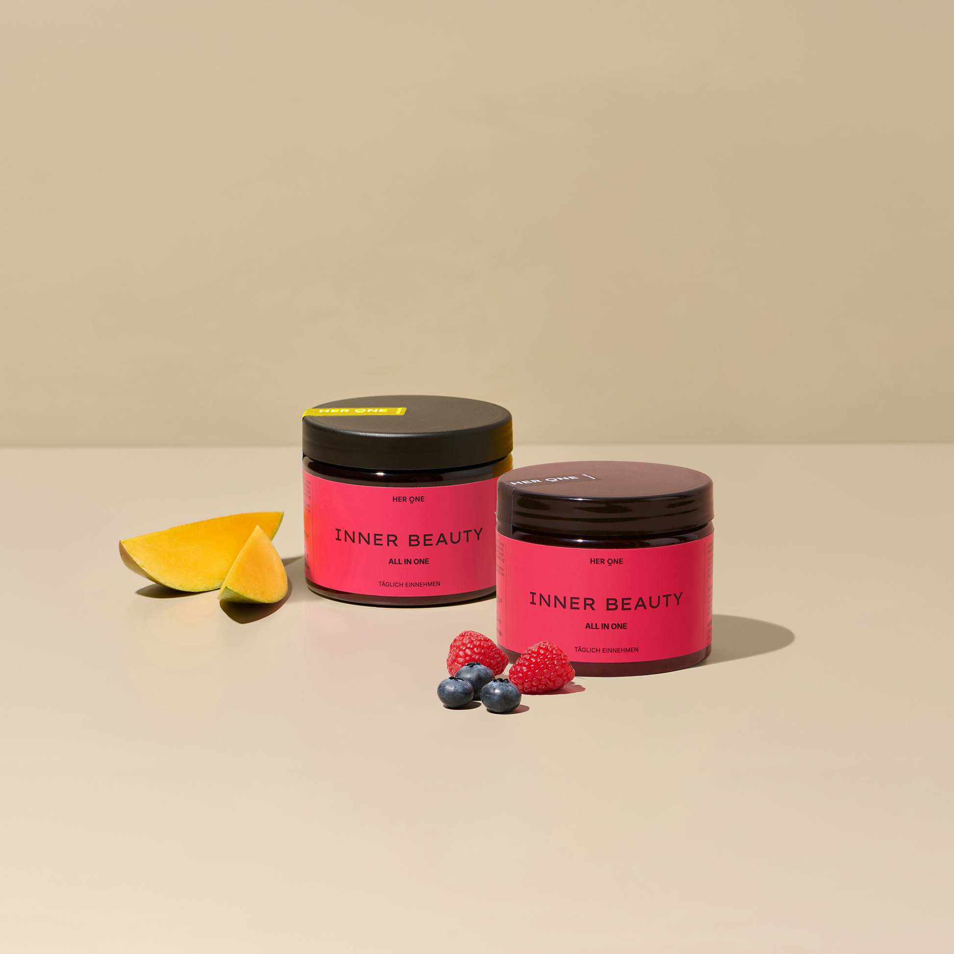 Two HER ONE Inner Beauty tins stand on a beige background, decorated with mango, raspberries and blueberries.