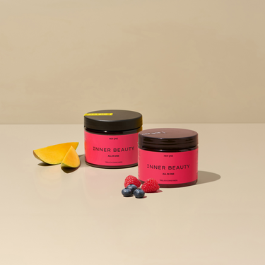 Two HER ONE Inner Beauty tins stand on a beige background, decorated with mango, raspberries and blueberries.
