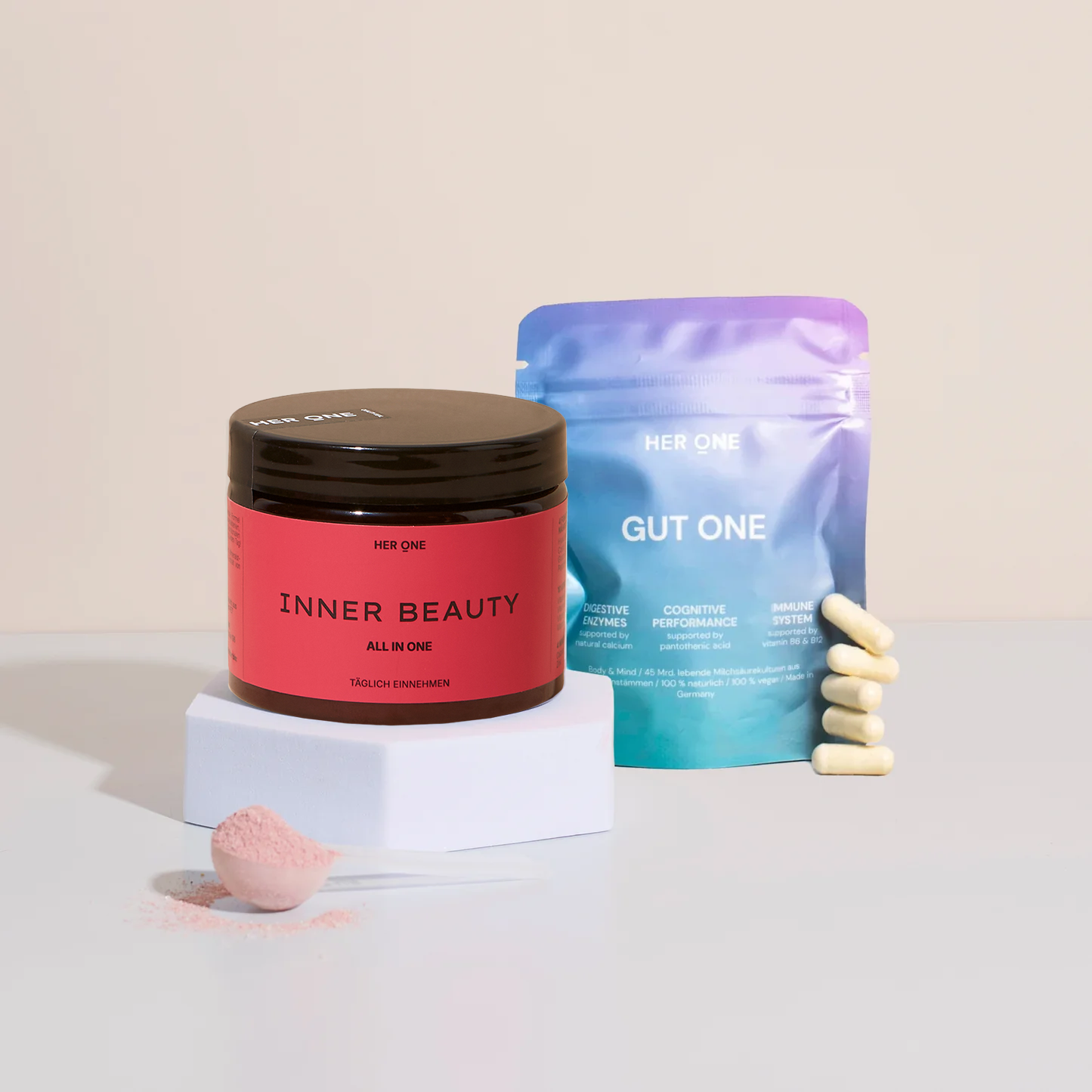 HER ONE INNER BEAUTY tin and GUT ONE sachet with capsules and powder on a light-colored base.