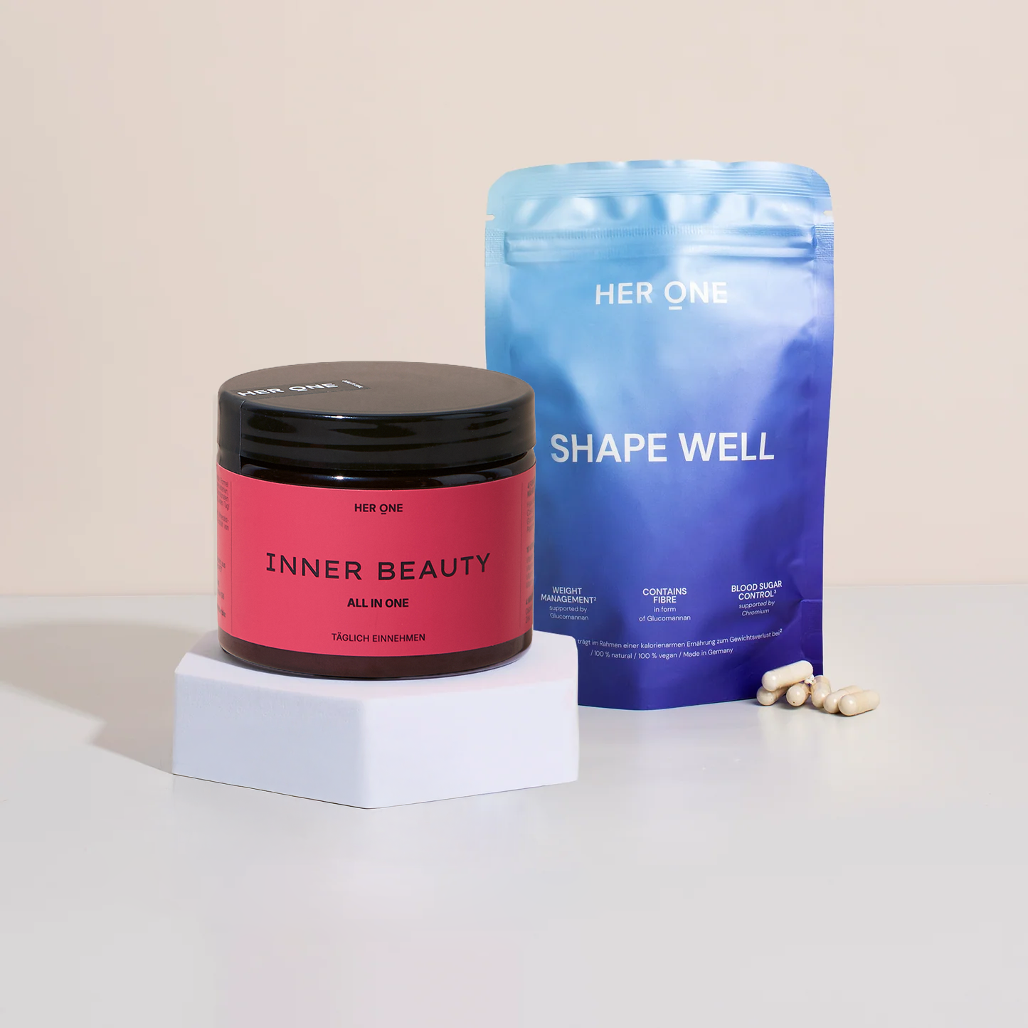 HER ONE INNER BEAUTY tin and SHAPE WELL sachet with capsules arranged on a light-colored base.