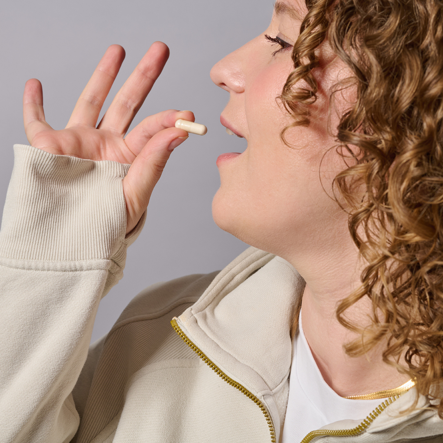 Person occupies a white capsule worn in beige clothing against a gray background.