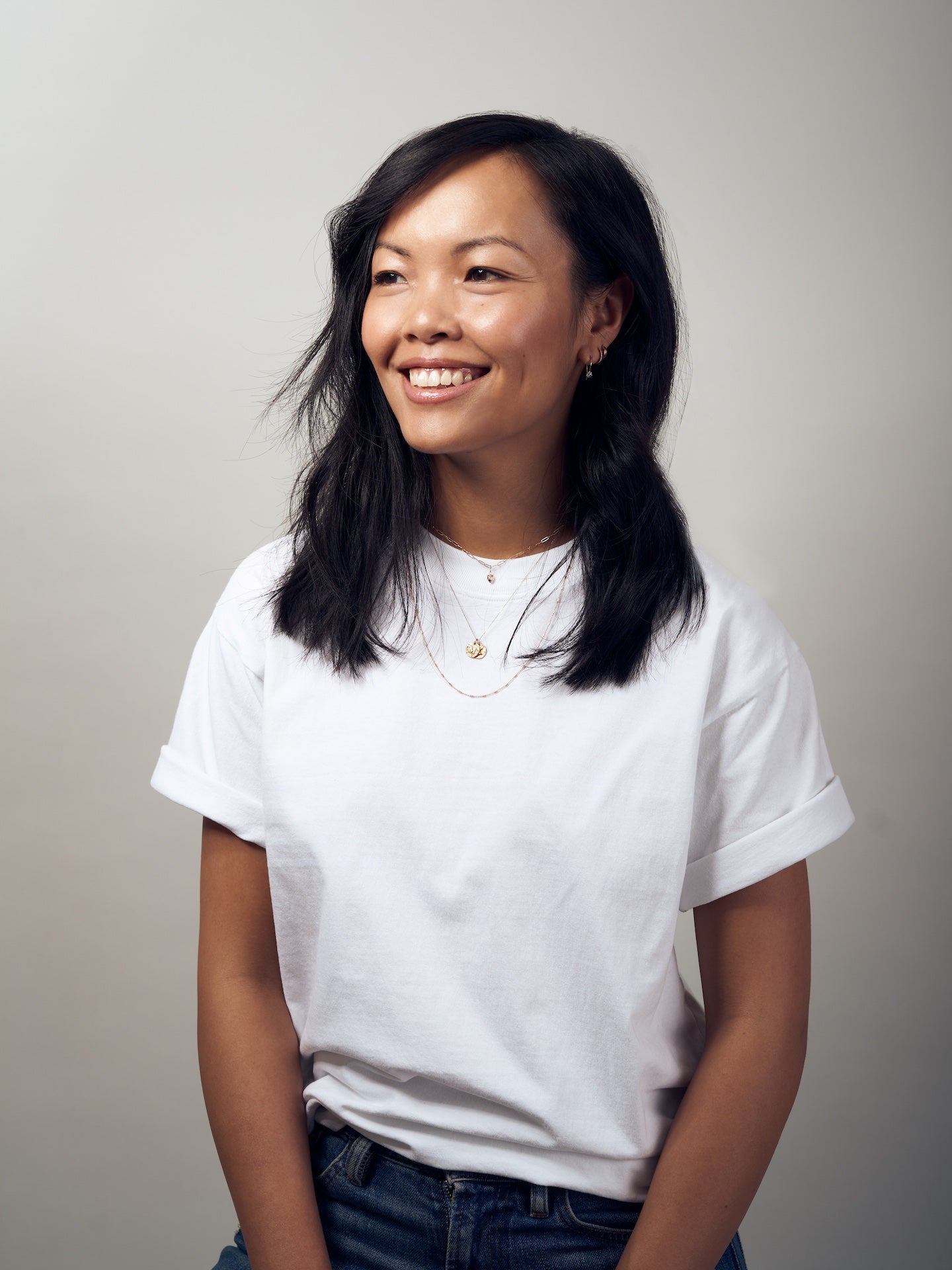 Rêve souriant avec des cheveux foncés et un T-shirt blanc sur un fond neutre.