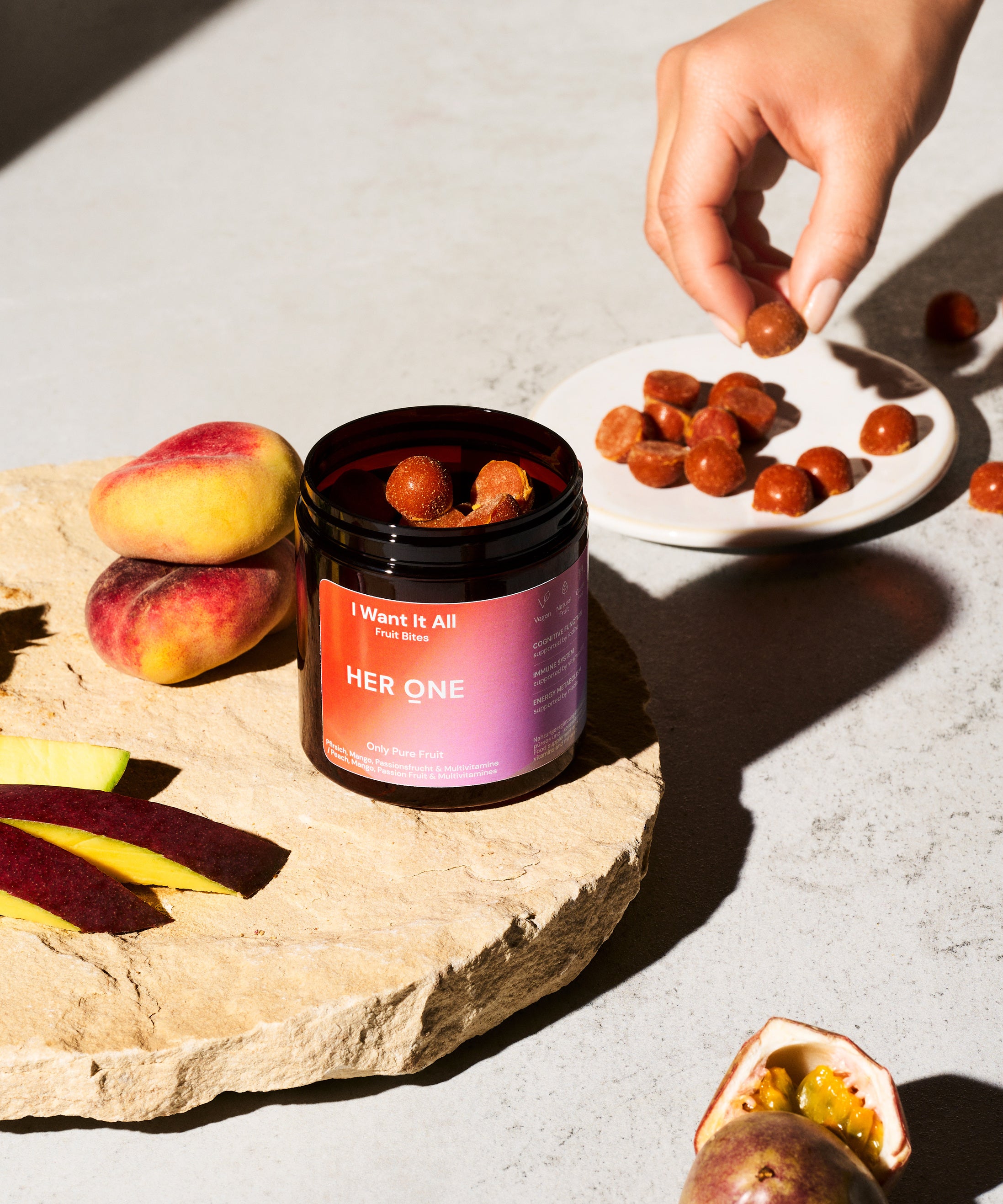 Une main saisit un snack fruité dans une assiette, à côté d'un récipient portant l'inscription "IWantItAll".