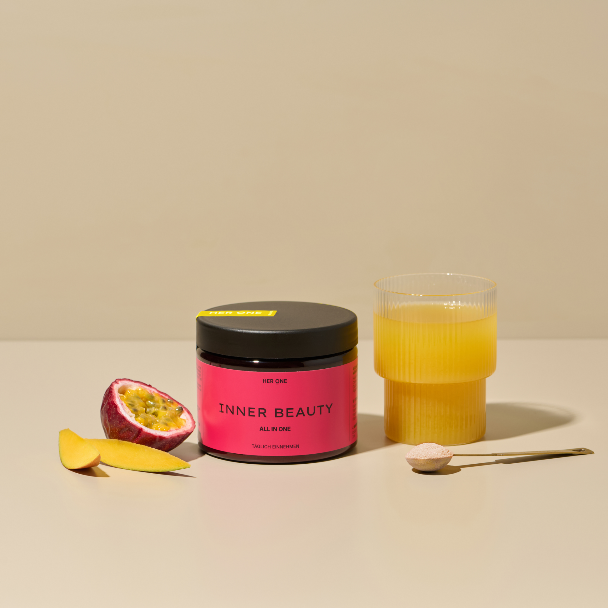 L'image montre INNER BEAUTY All in One au goût de mangue et de fruits de la passion. À côté du produit, on voit une mangue coupée et un demi-fruit de la passion. Dans un verre à droite de l'image, la boisson est mélangée et présentée avec une cuillère pleine d'INNER BEAUTY devant.
