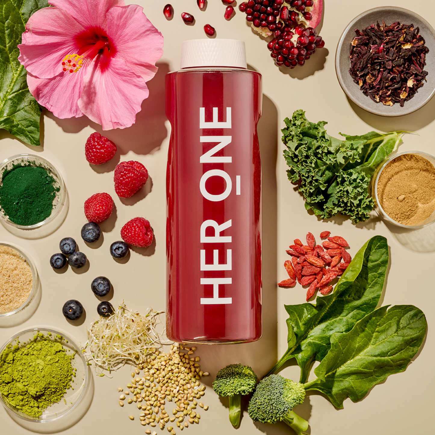 Une bouteille rouge avec l'inscription "HER ONE" entourée d'ingrédients à base de fruits et de légumes sur un fond clair.