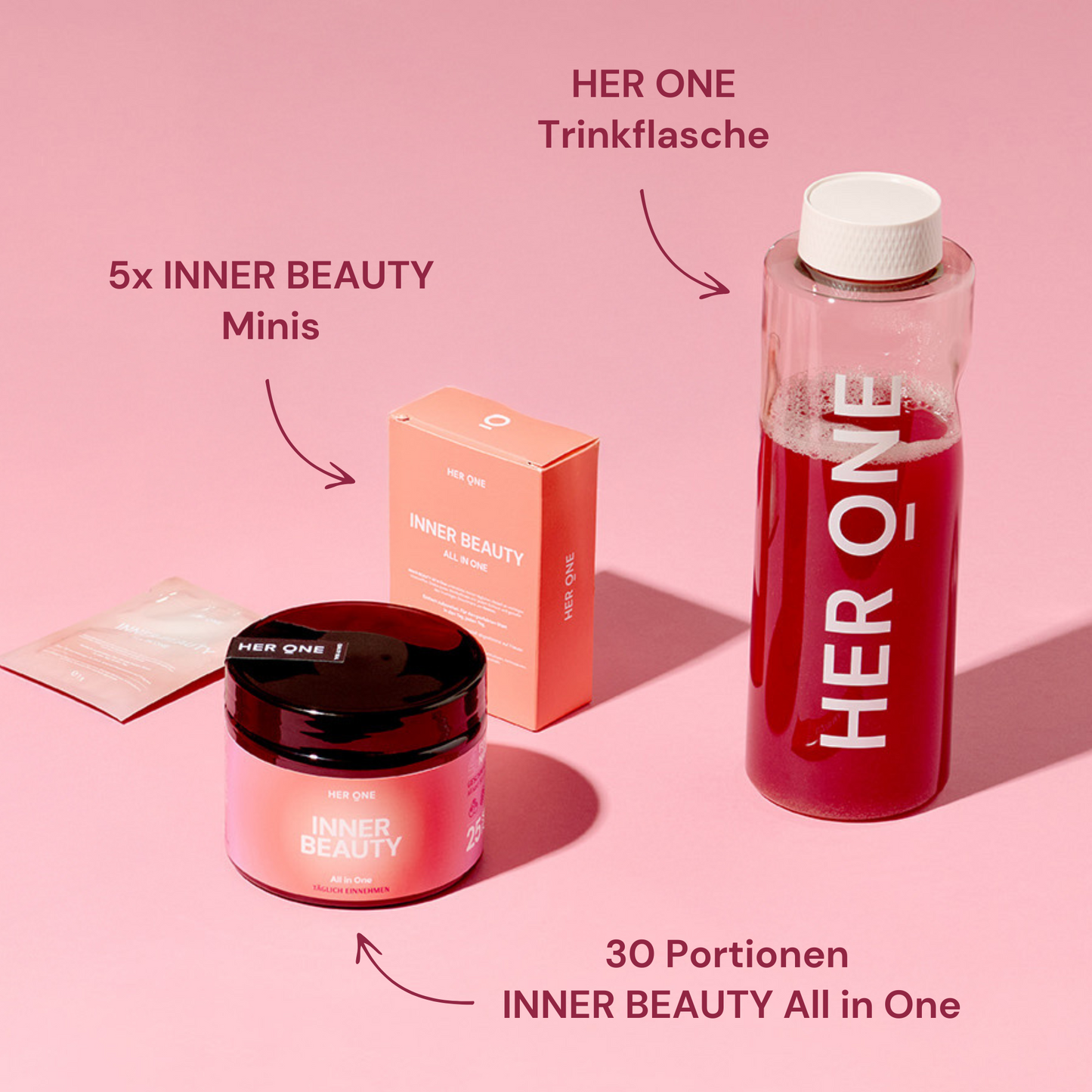 Photo de produit avec bouteille HER ONE, verre INNER BEAUTY , boîte et paquets individuels sur fond rose.