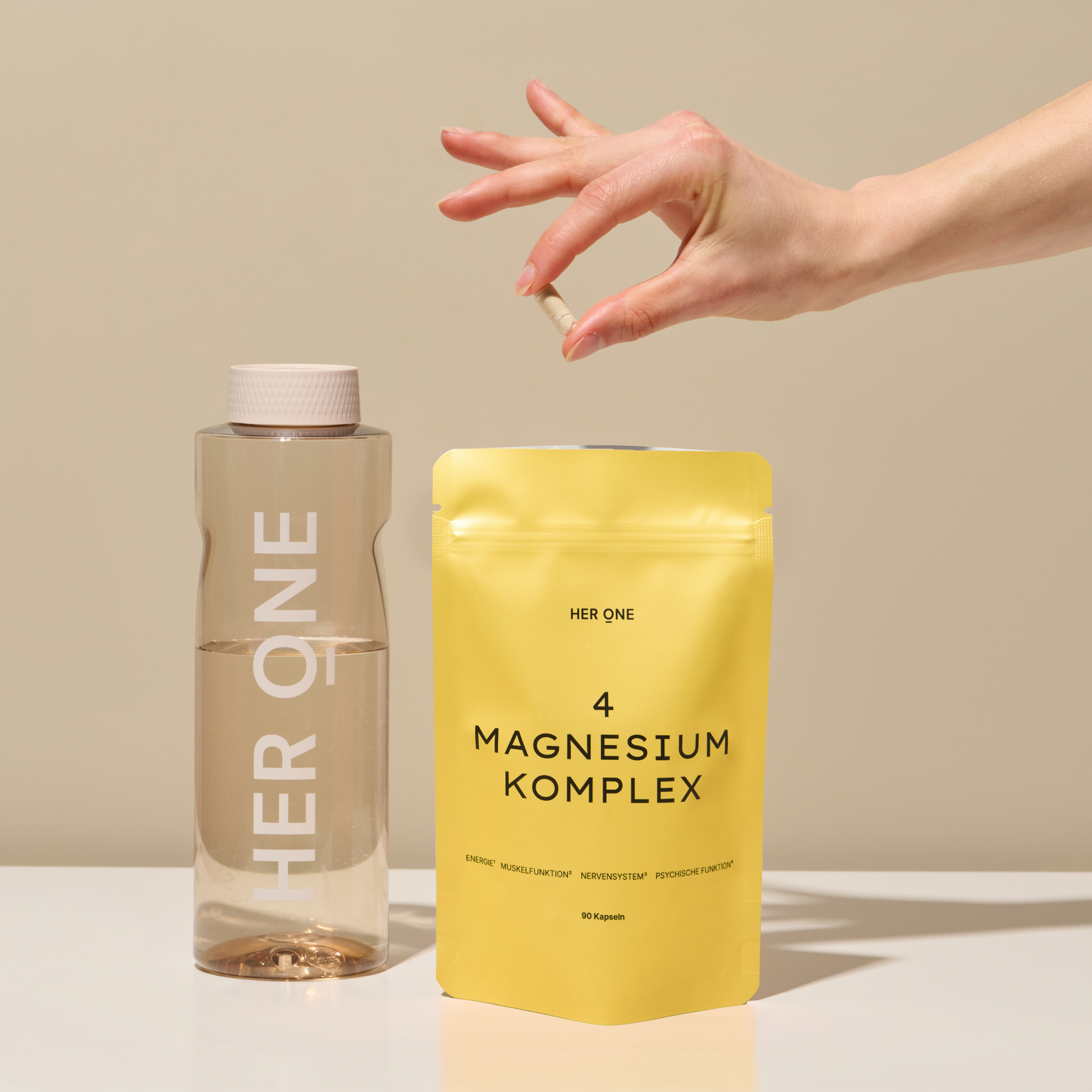 Une main tient une capsule au-dessus d'un emballage jaune de complexe de magnésium à côté d'une bouteille d'eau sur une table.