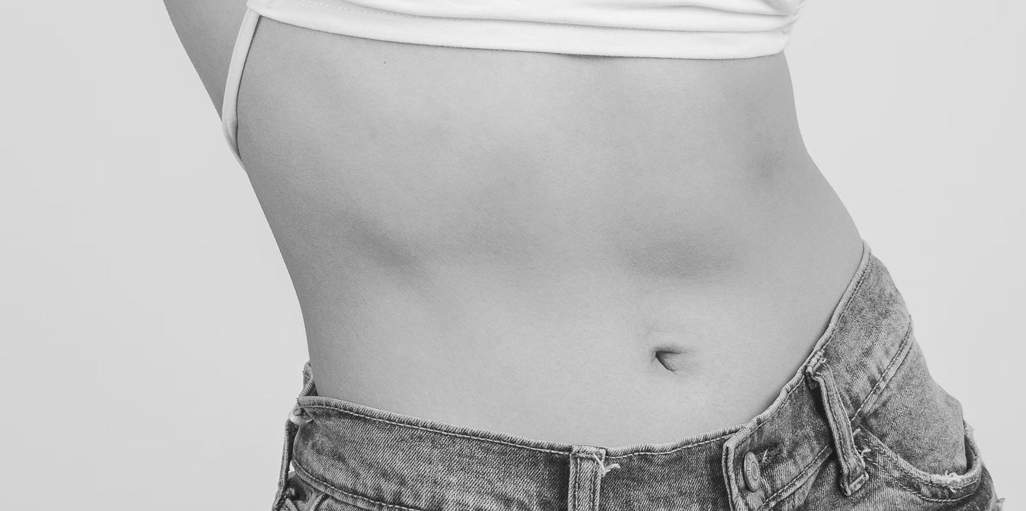 Primo piano di una pancia scoperta in top e jeans bianchi.