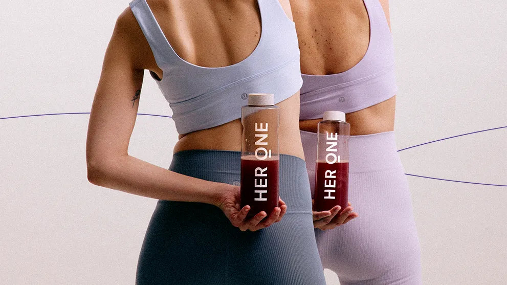 Twee mensen in sportkleding houden flessen met de tekst "HERONE" in hun handen achter hun rug.