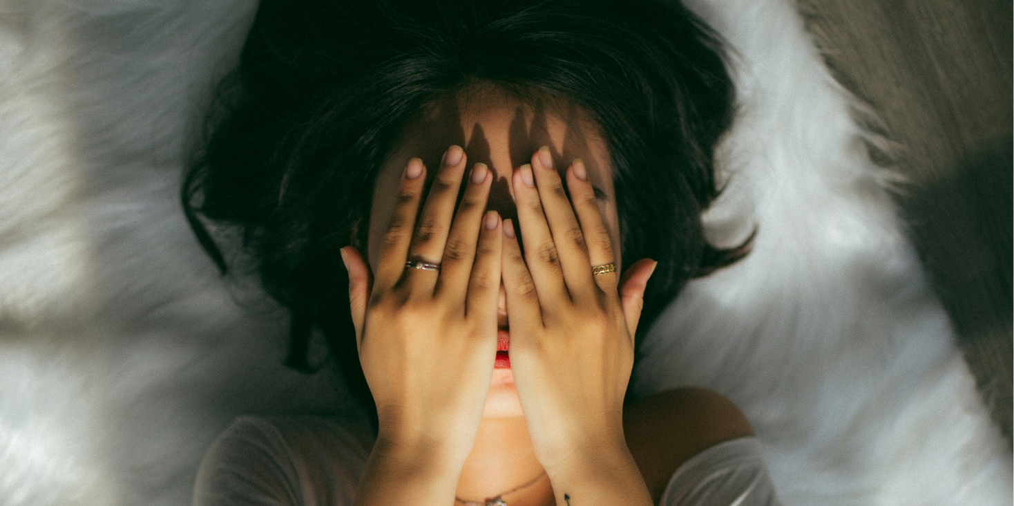 La persona si sdraia su un tappeto di pelliccia bianca e si copre il viso con entrambe le mani.