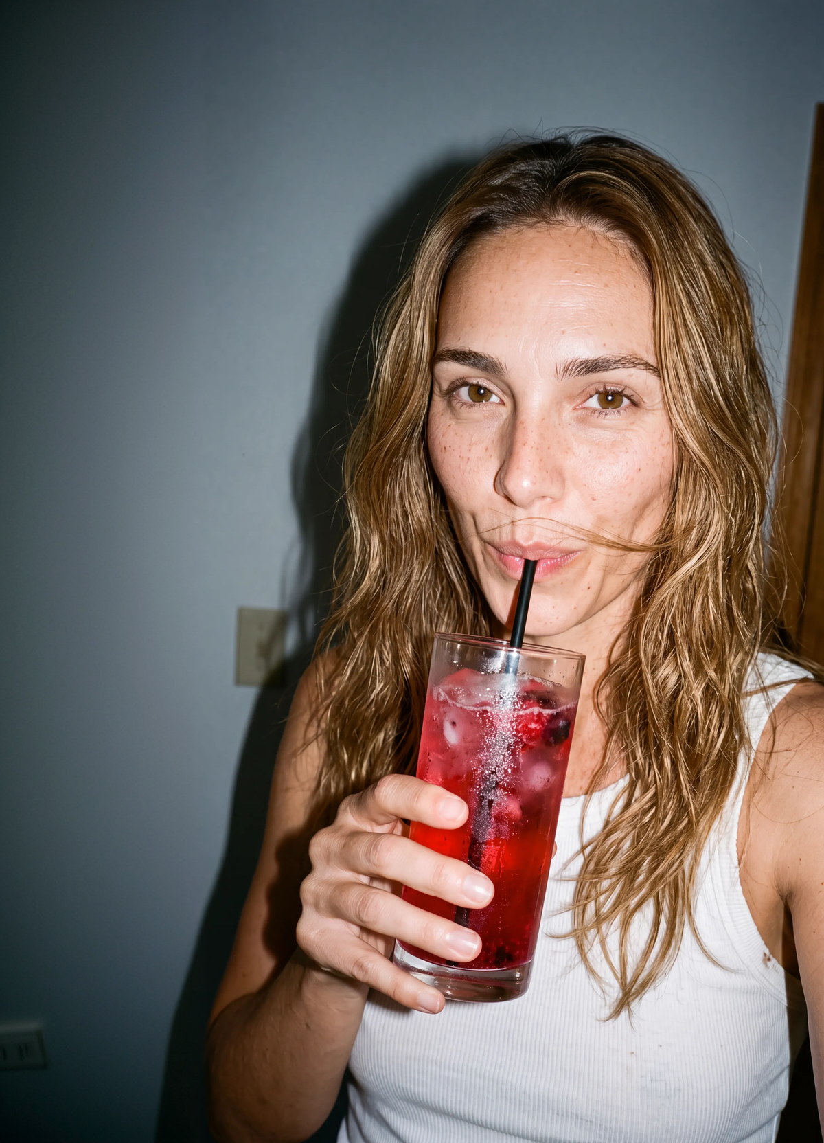 Frau in weißem Top trinkt roten Drink mit Strohhalm aus einem Glas.