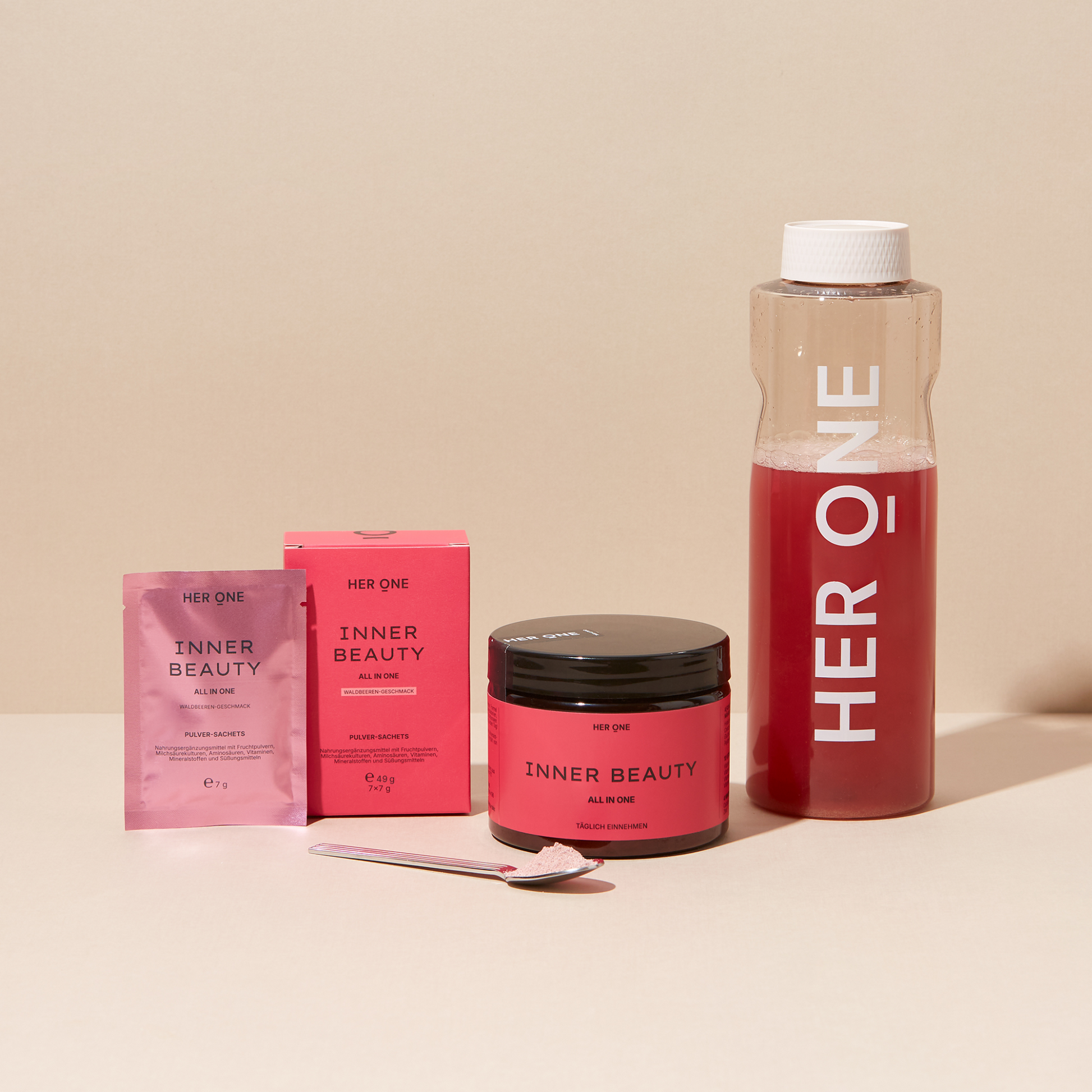 Produkte der Marke "HER ONE" mit einem Glas, einer Schachtel und einem Löffel auf einem beigen Hintergrund.