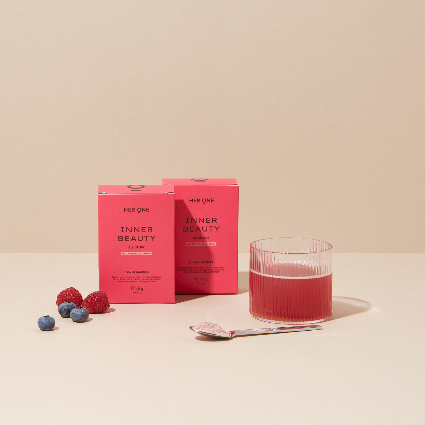 Zwei Packungen Inner Beauty All in One Mini, ein Glas mit angemischtem Inner Beauty, ein Löffel mit Pulver sowie Beeren auf der linken Seite.