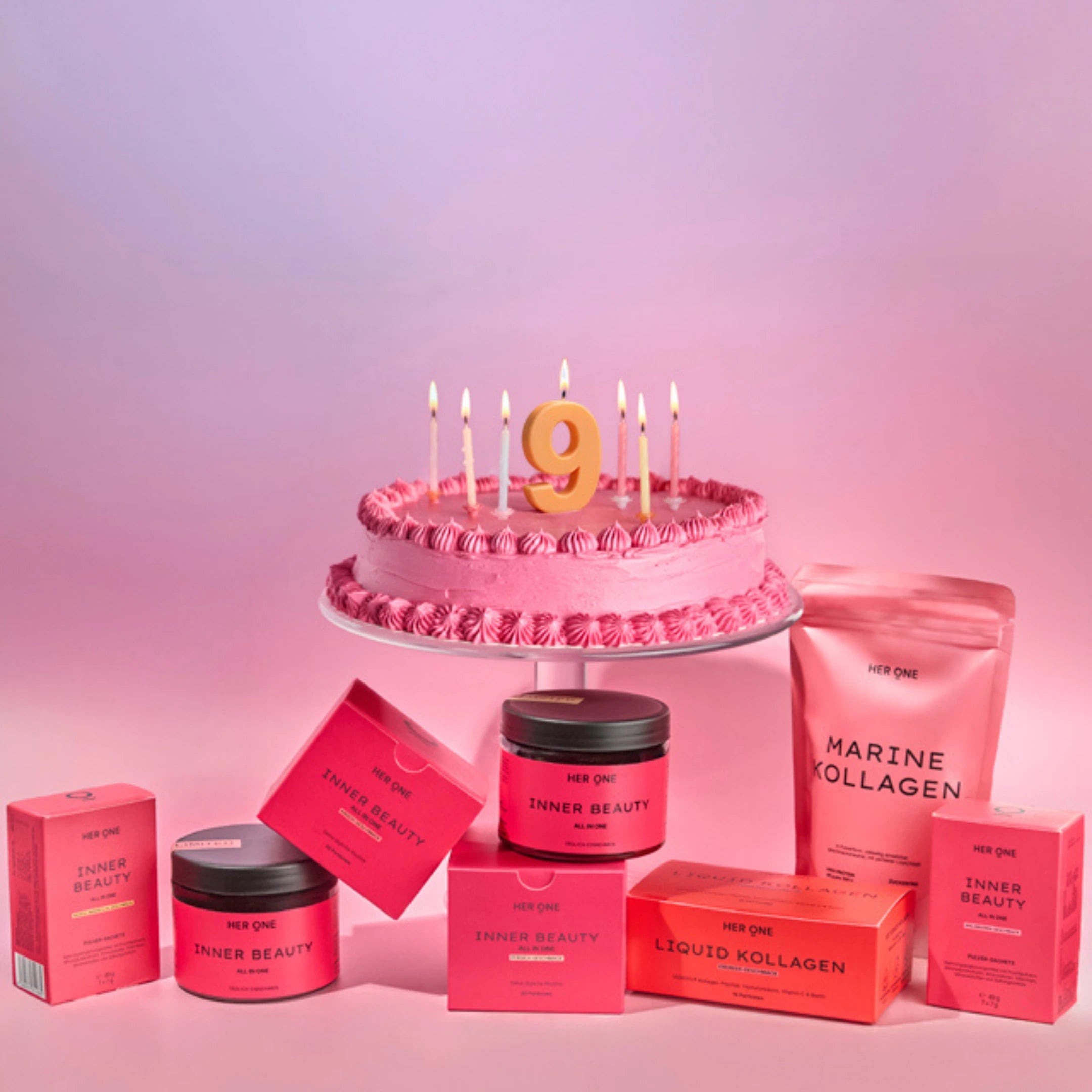 HER ONE Produkte vor einer Geburtstagstorte auf rosa-violettem Hintergrund.