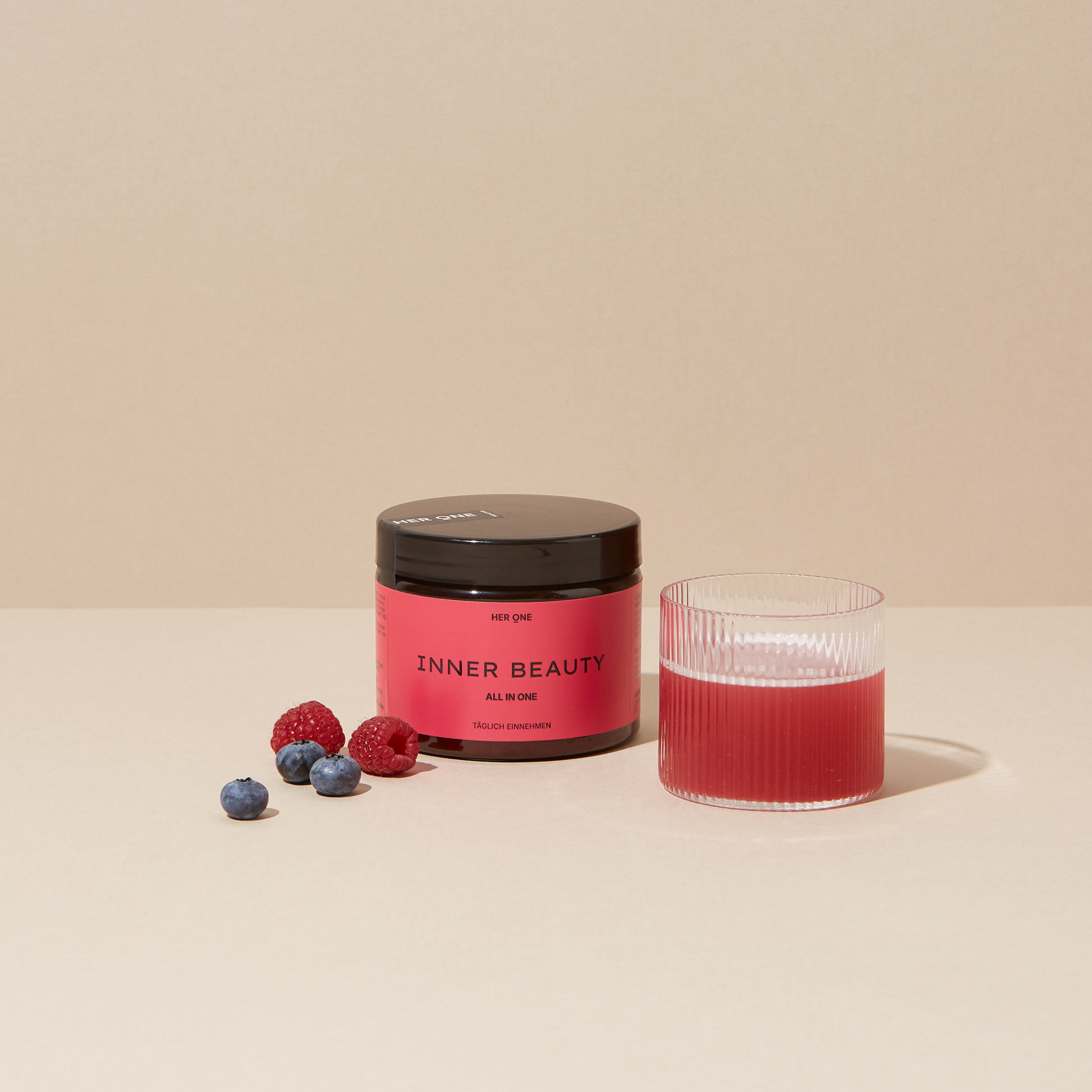 Ein Glas mit pinkem Getränk, ein Dosenglas "INNER BEAUTY", Himbeeren, Heidelbeeren und ein goldener Löffel mit Pulver.