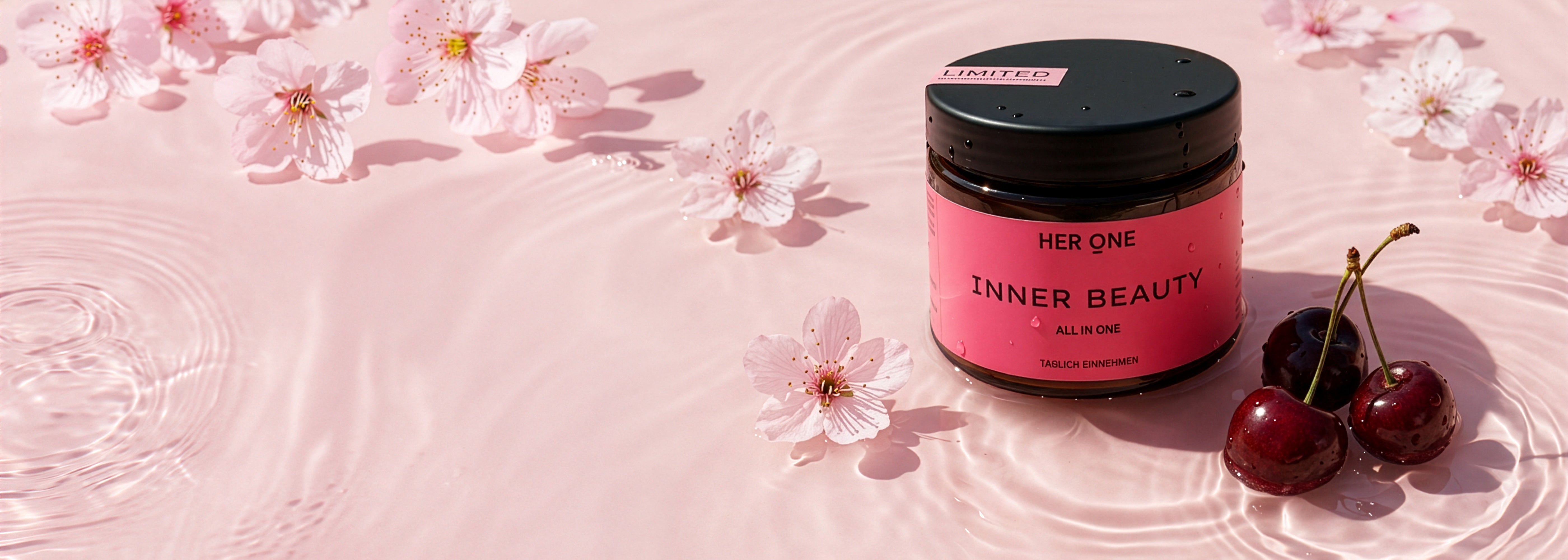 HER ONE Inner Beauty Dose im Wasser liegend, umgeben von Kirschen und rosa Kirschblüten vor hellem Hintergrund.