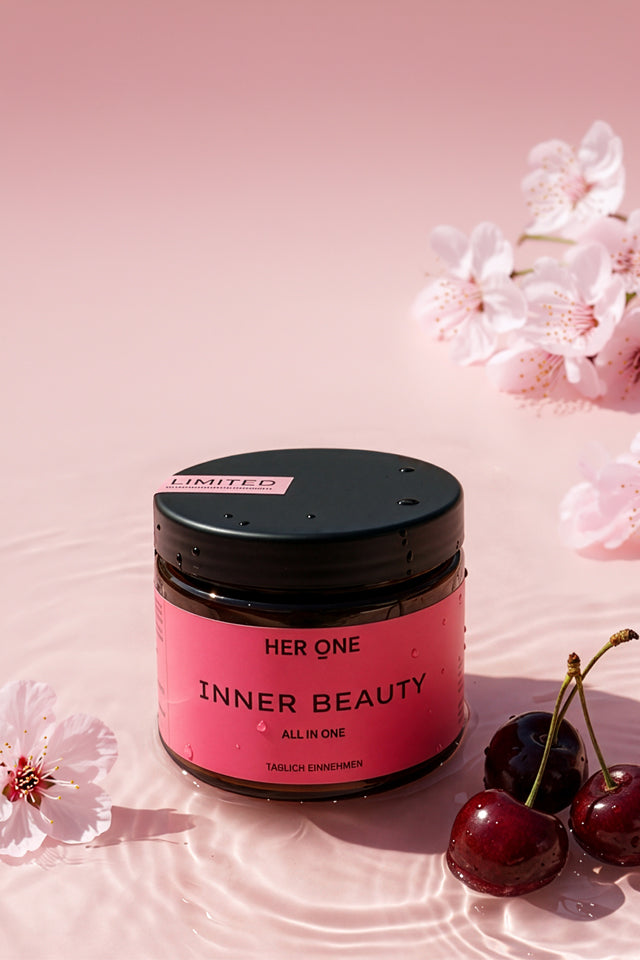 HER ONE Inner Beauty Dose im Wasser liegend, umgeben von Kirschen und rosa Kirschblüten vor hellem Hintergrund.