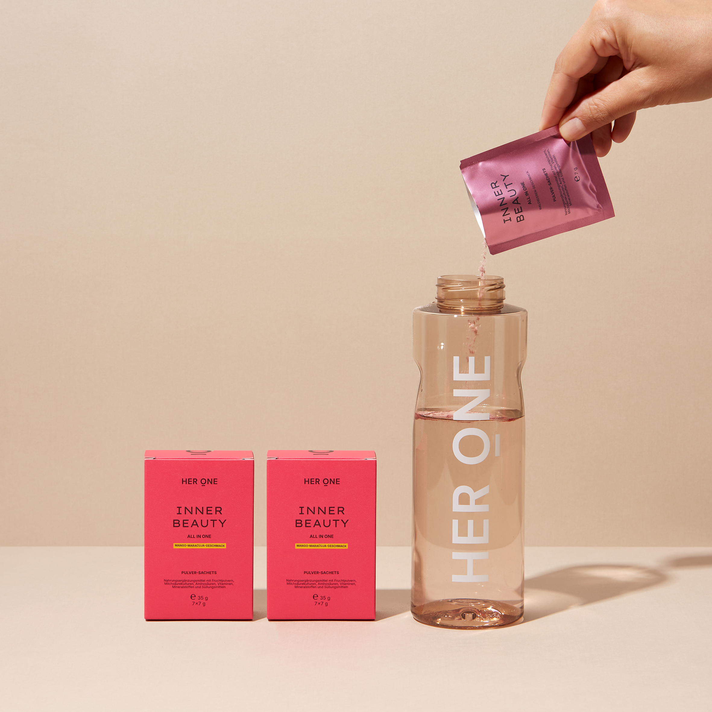 Un sachet INNER BEAUTY versé dans une gourde HER ONE ; à côté se trouvent deux paquets Inner Beauty in One Minis Mangue-Framboise