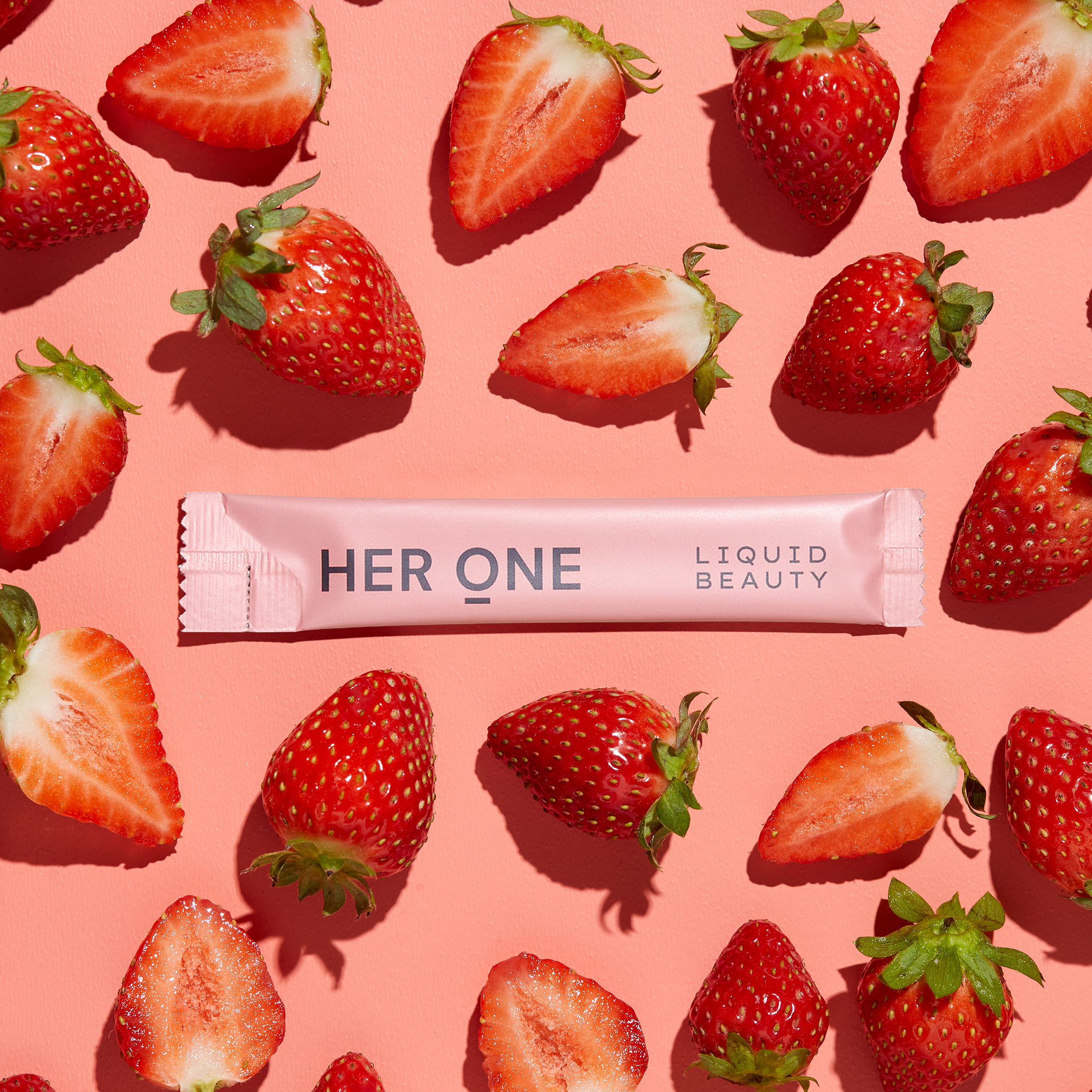 HER ONE Liquid Beauty Stick liegt zwischen frischen und halbierten Erdbeeren auf rosa Hintergrund.
