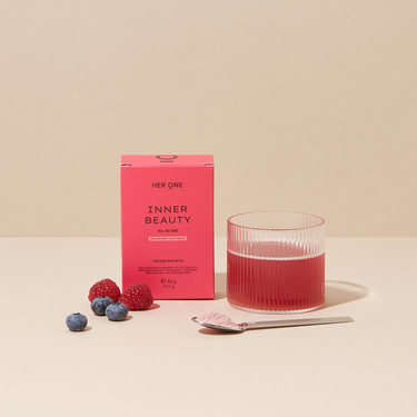 Ein Glas mit rotem Getränk, eine Packung "Inner Beauty", frische Beeren und ein Löffel mit Pulver auf einem Tisch.
