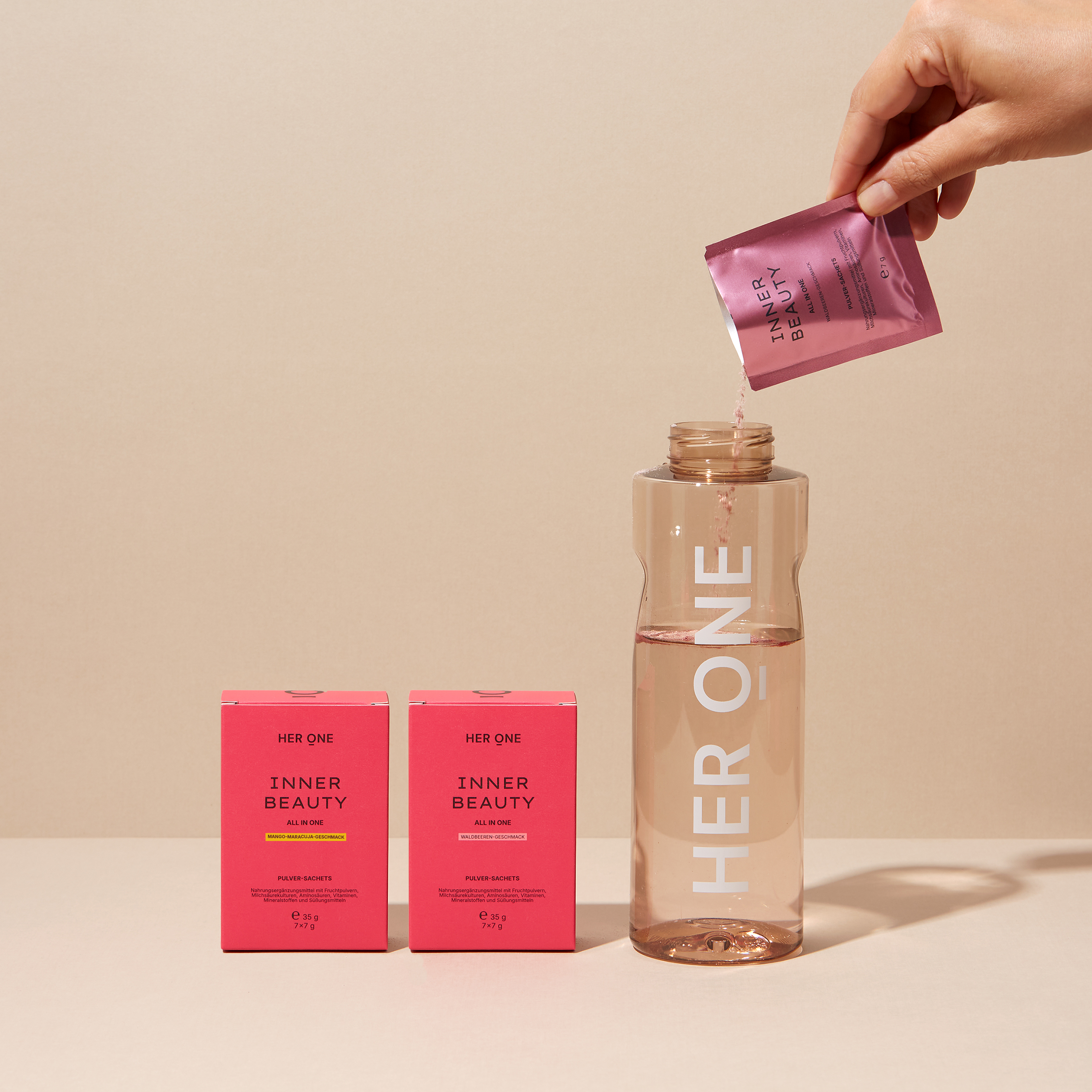 Un sachet INNER BEAUTY versé dans une gourde HER ONE ; à côté se trouvent deux boîtes Inner Beauty in One : Baies des bois & Mangue-fruit de la passion