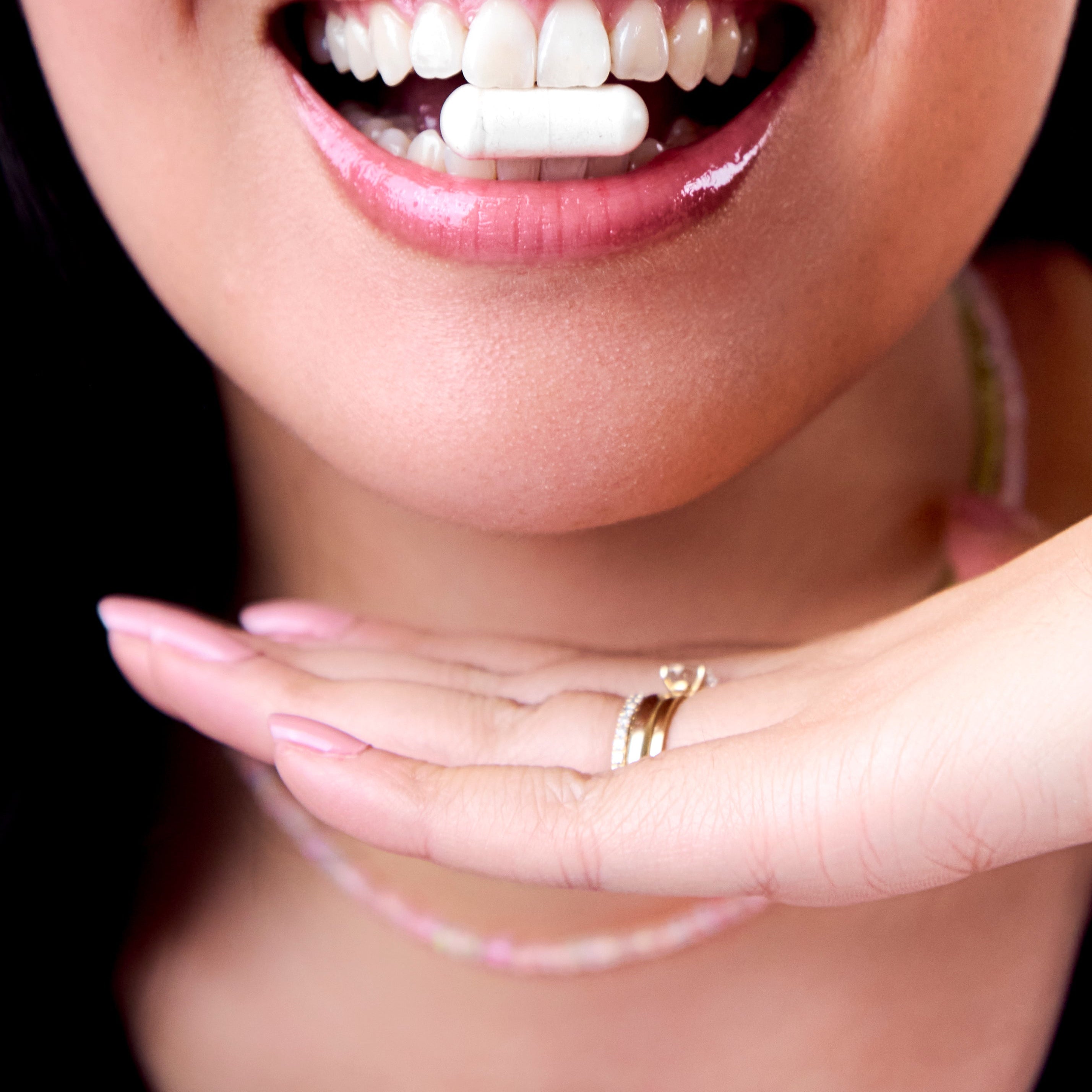 Woman smiling showing healthy teeth holding HER ONE Gut One capsule
