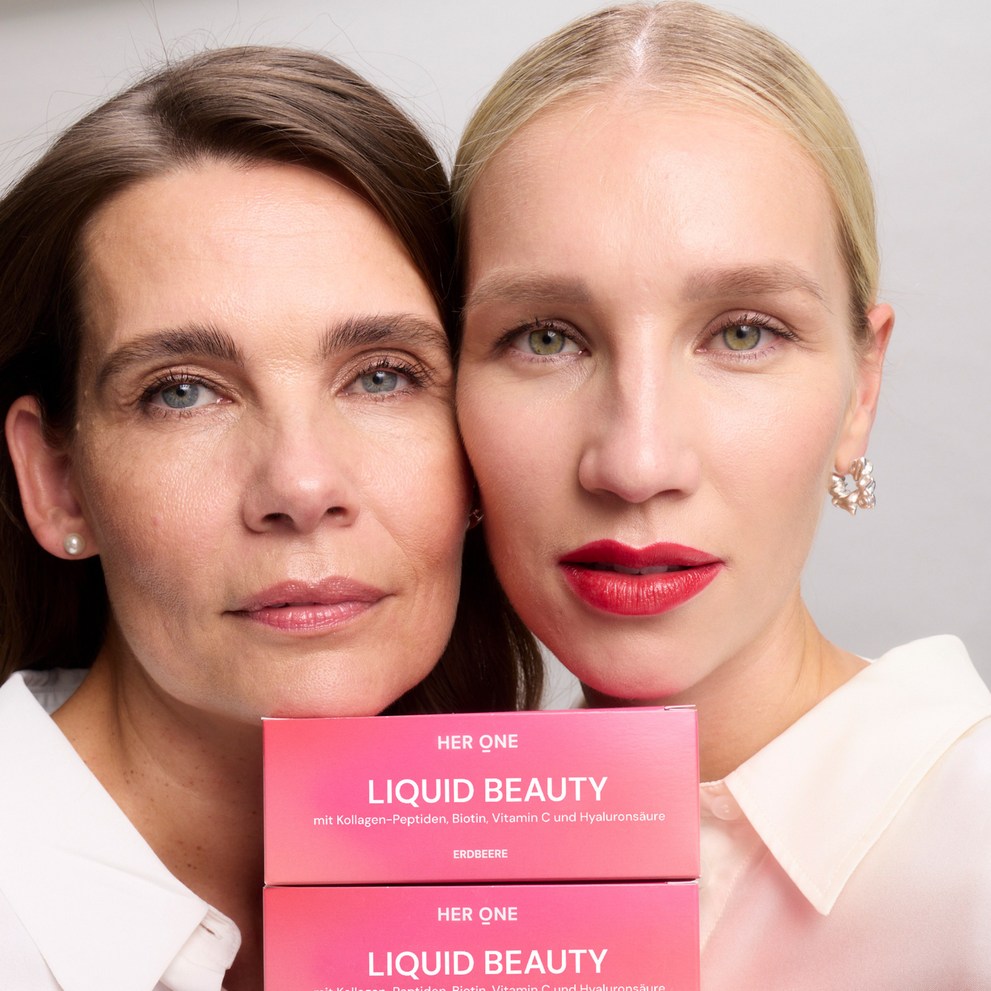 Two women hold boxes labeled "Liquid Beauty" up to the camera, the product is from Her One.