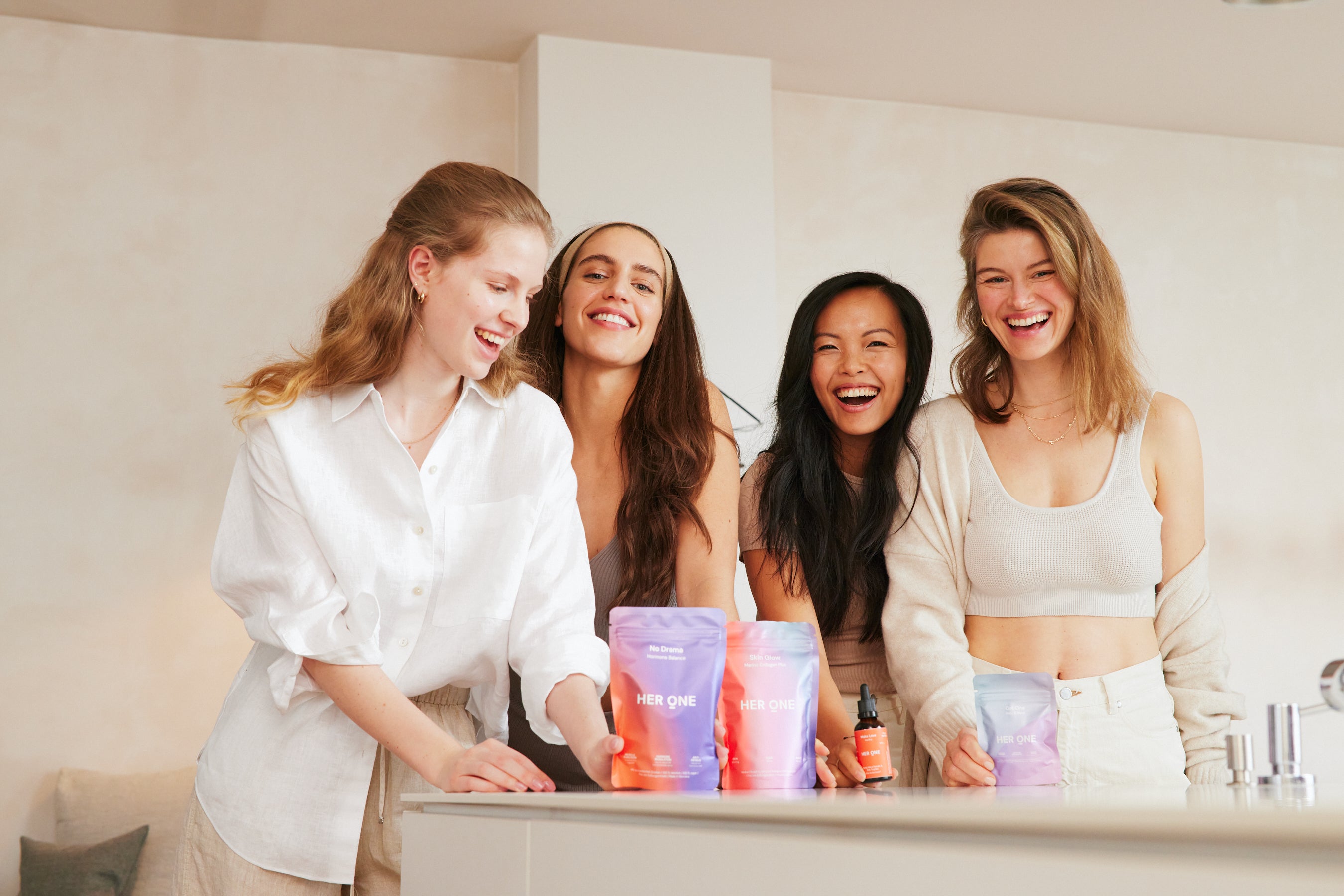 Four smiling women stand in bright clothes at a table with products from "HERONE".