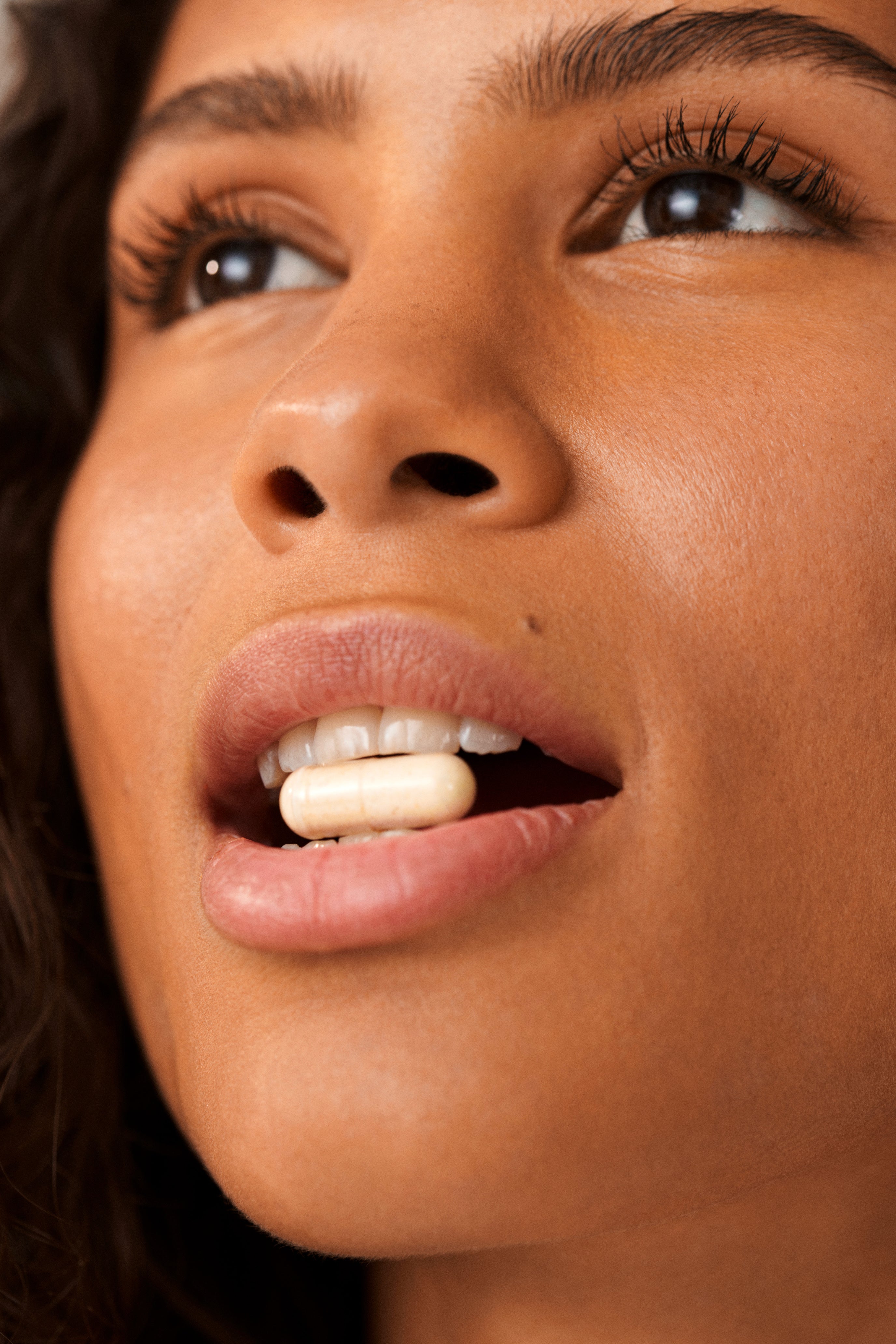 Close-up of a face with a person holding a white capsule in their mouth.