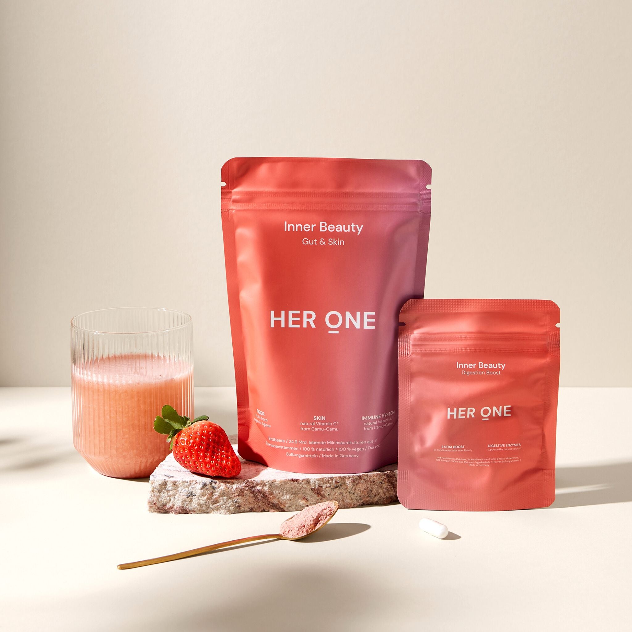 Two red packages labeled "Inner Beauty HERONE", a glass of juice, a strawberry and a spoon.
