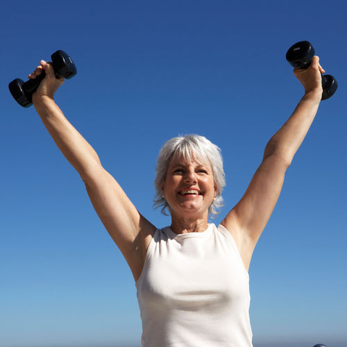 Elderly woman lifts dumbbells in sunny weather and smiles.