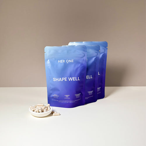 Three blue packages labeled "ShapeWell" stand behind a tray with white capsules on a table.