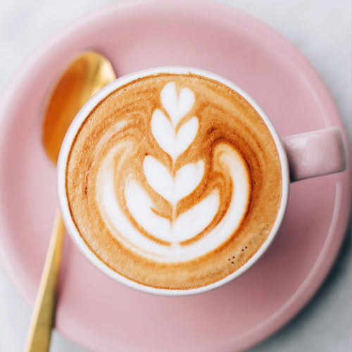 Cappuccino with latte art in a pink cup on a matching plate with a golden spoon.