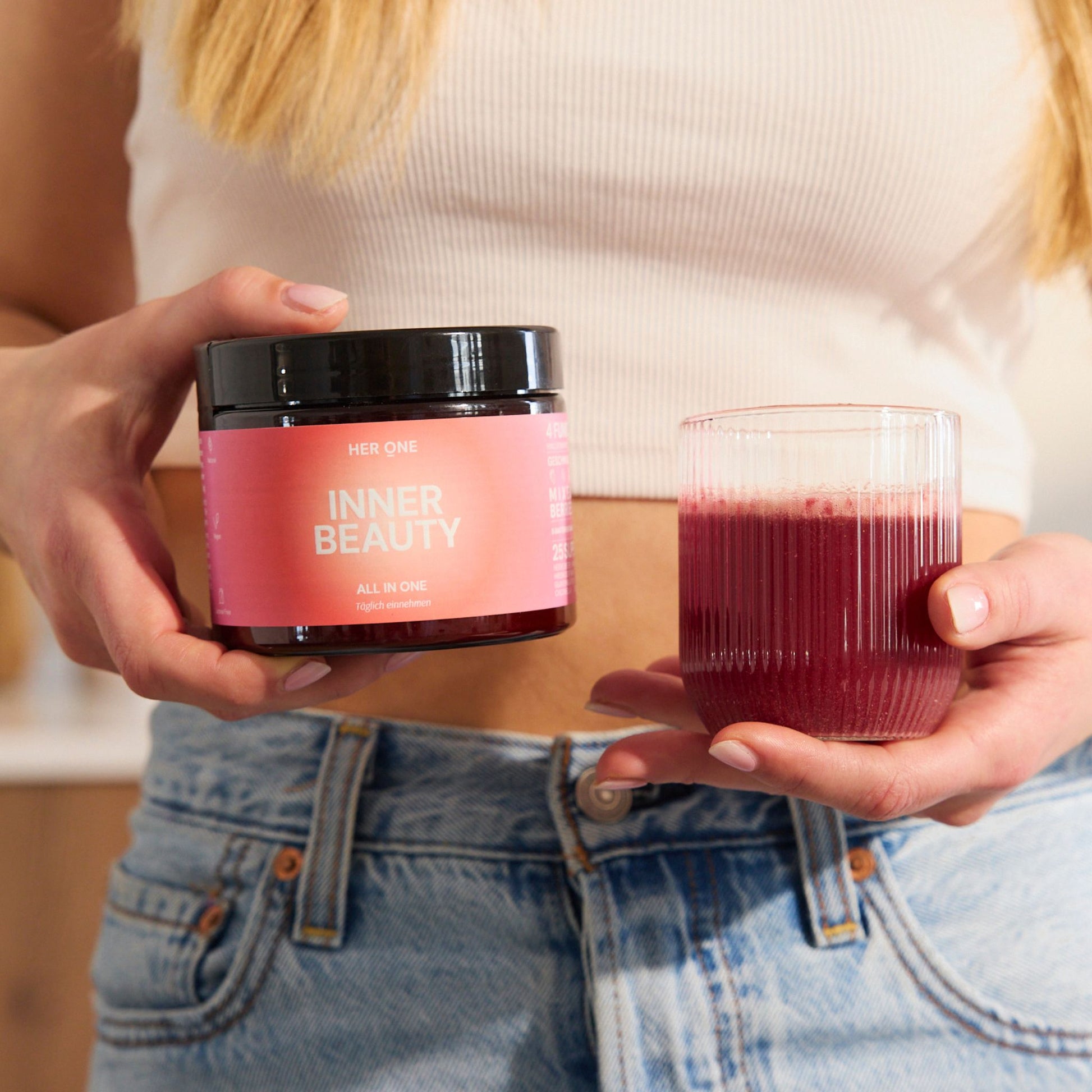 Woman holding a glass with red drink and a container with pink labelInner Beauty".