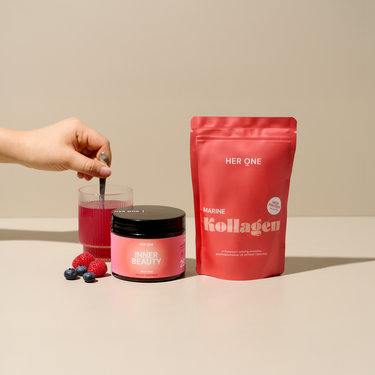 A hand stirs in a glass of pink drink. In front of it are an Inner Beauty, a collagen bag and berries.
