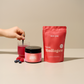 A hand stirs in a glass of pink drink. In front of it are an Inner Beauty, a collagen bag and berries.