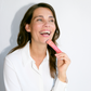 Woman in white shirt laughing and holding a pink product labeled "LIQUID BEAUTY".