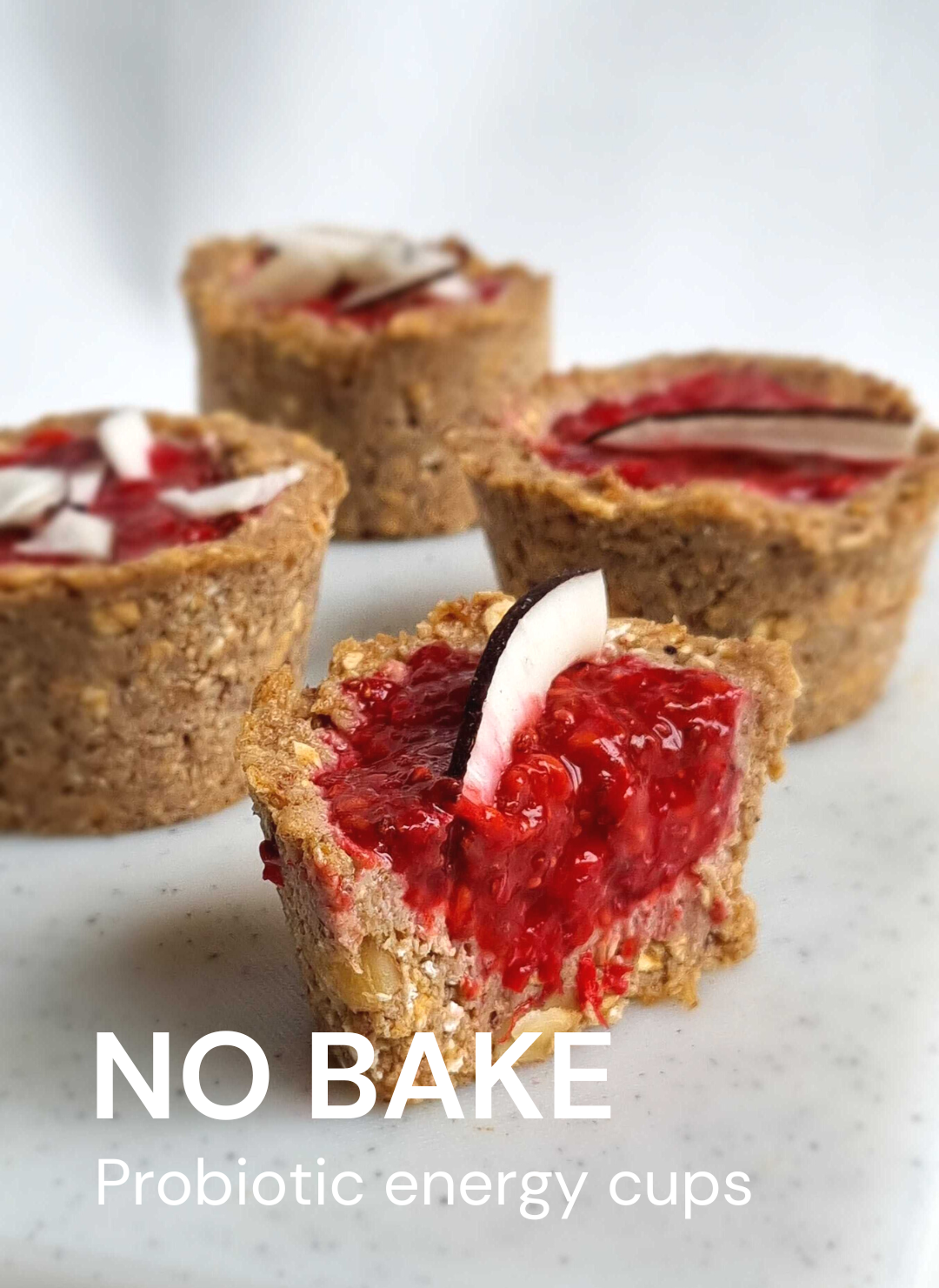 Four vegan, probiotic energy cups with red berries and coconut pieces on a white plate. text: "NOBAKE".
