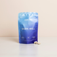 A blue product bag with the wordsShape Well" and some white capsules in front of it on a table.