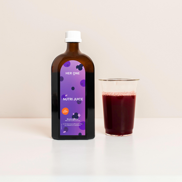 Brown bottle with purple label next to a glass of red juice on a white background.