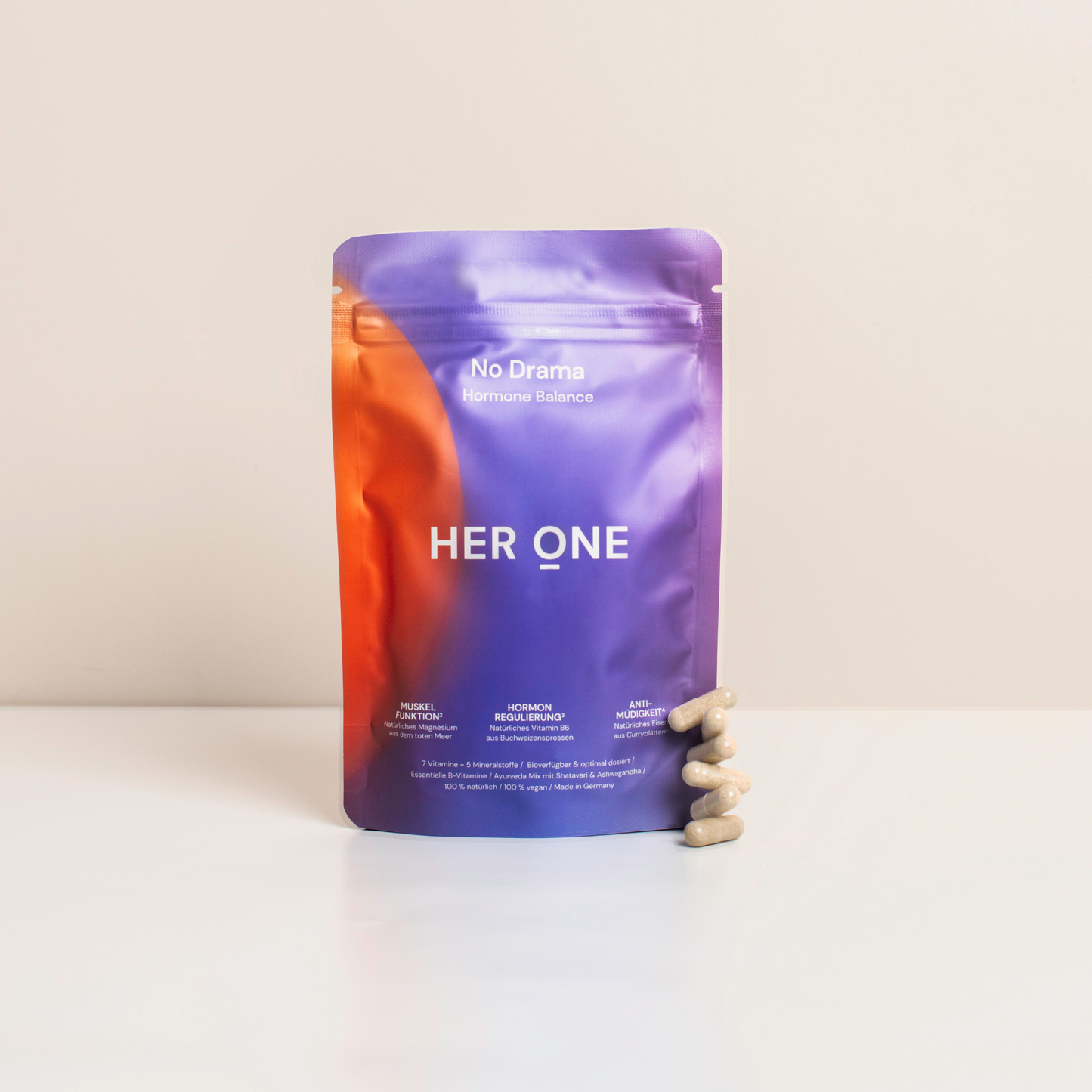 Packaging labeled "HER ONE" in purple and orange, with several capsules lying on a table next to it.