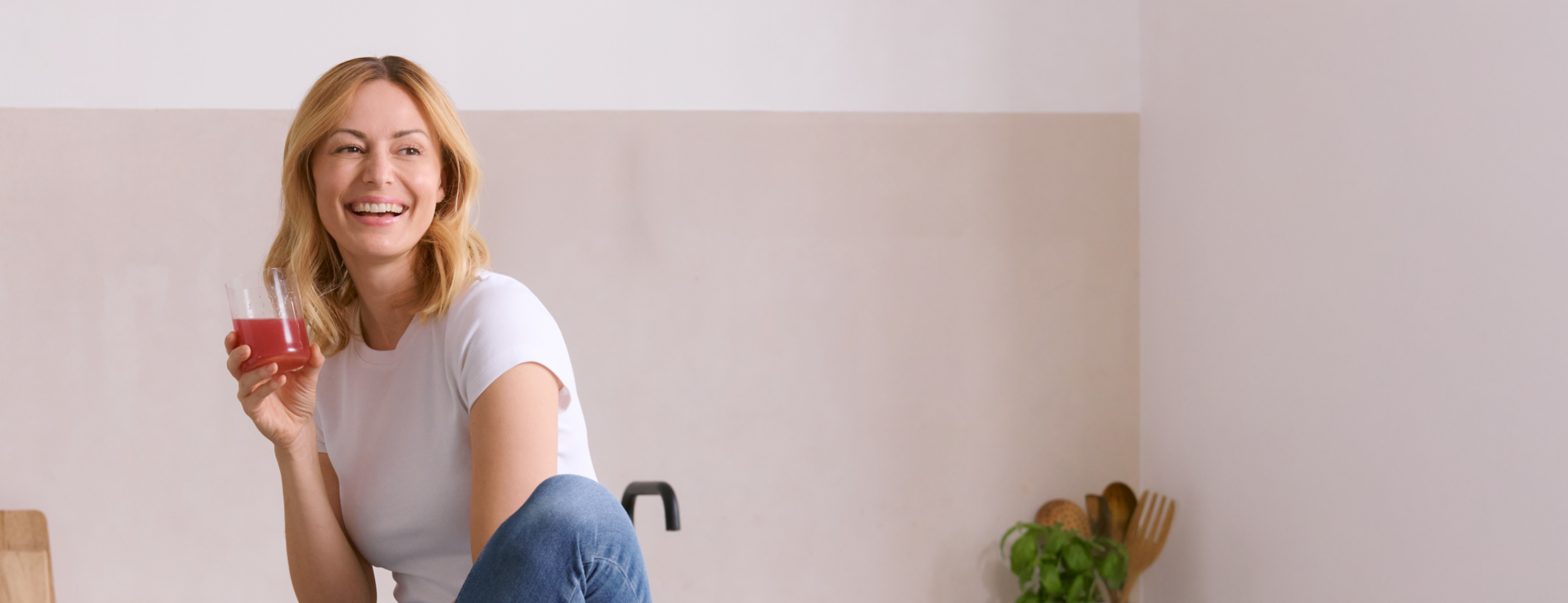 Laughing woman sitting in the kitchen with a glass of red drink, fresh and natural lifestyle moment
